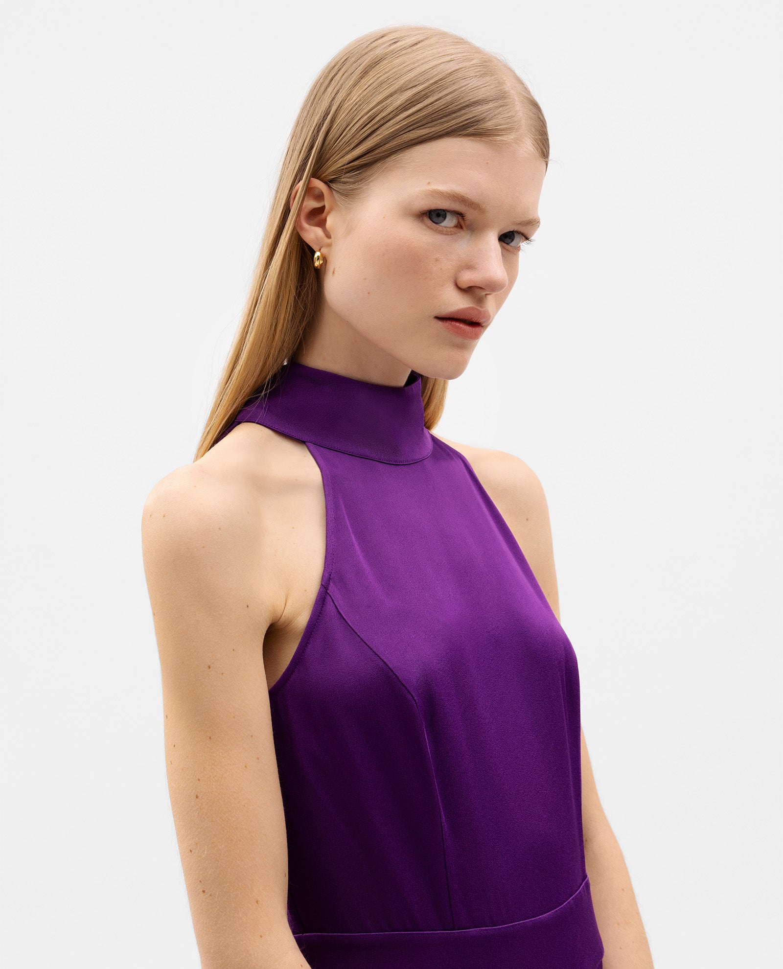 A woman with long blonde hair models the IVY OAK PHILIPPINE Jumpsuit, featuring a sleeveless design and stand collar in purple satin, against a plain background.