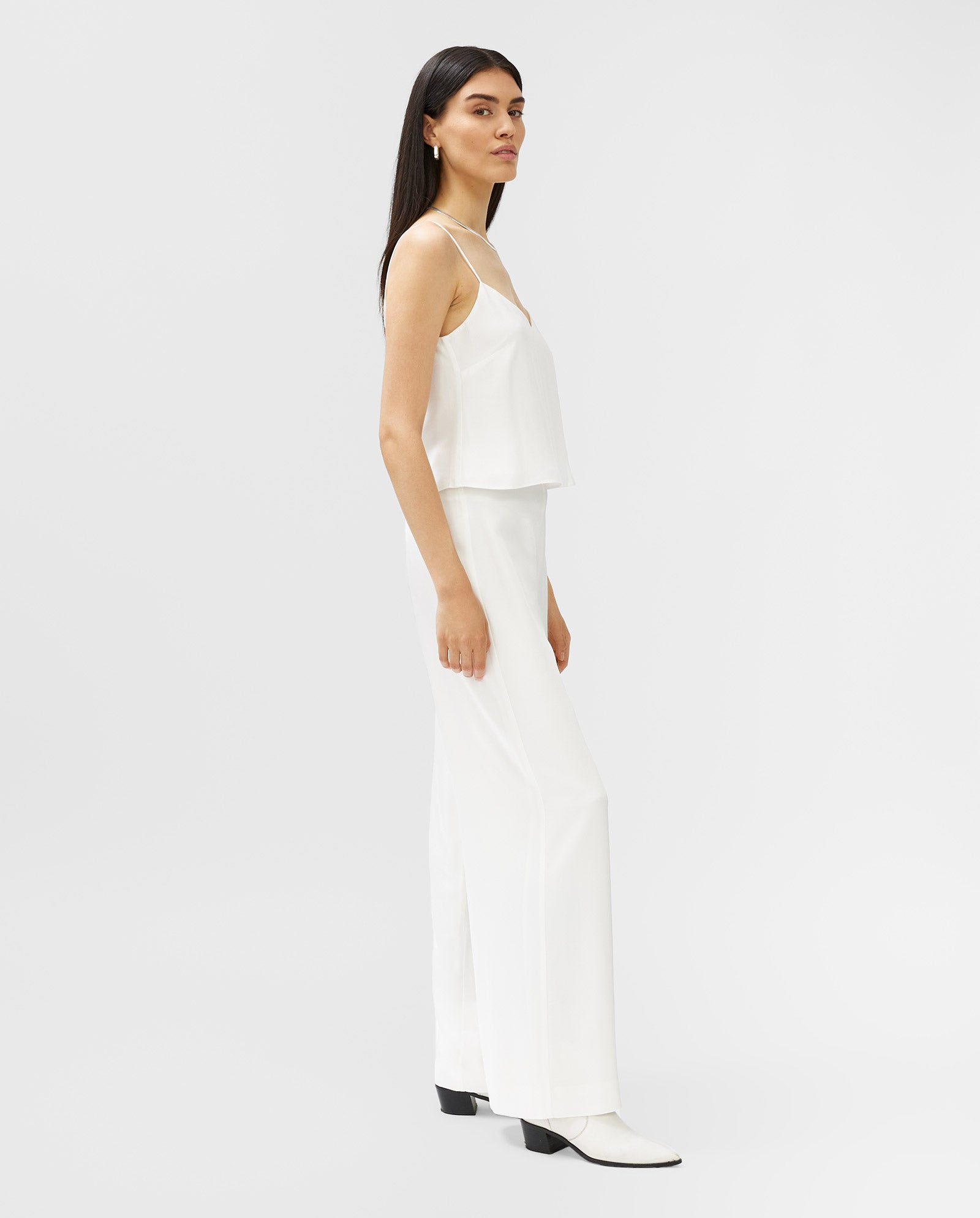 A woman stands sideways against a plain light background, wearing IVY OAKs PETUNIA Trouser paired with a white sleeveless top.