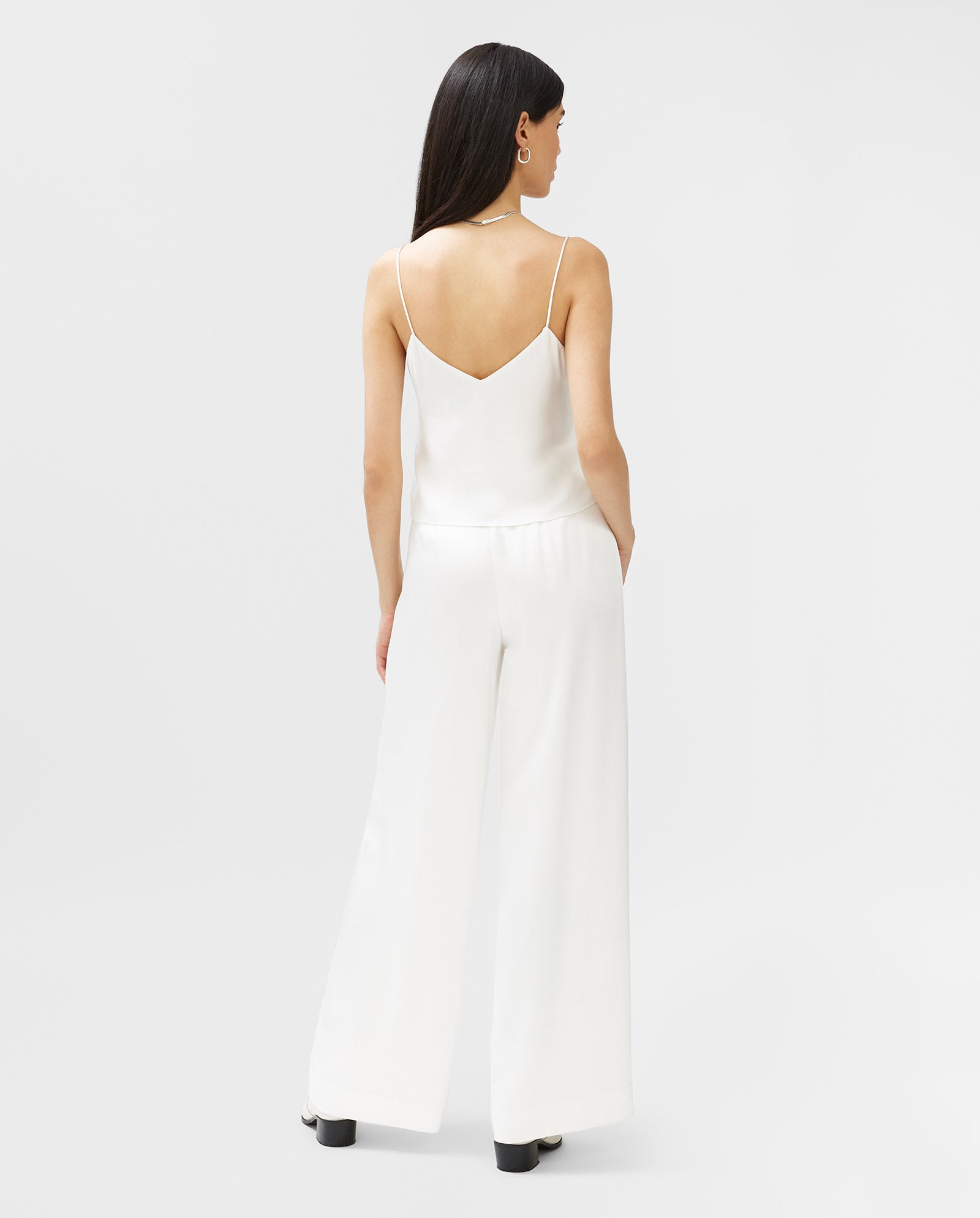 A woman stands with her back to the camera, wearing IVY OAKs PETUNIA Trouser—wide-leg, high-waist pants crafted from a soft Viskose Mix—and a sleeveless white top.