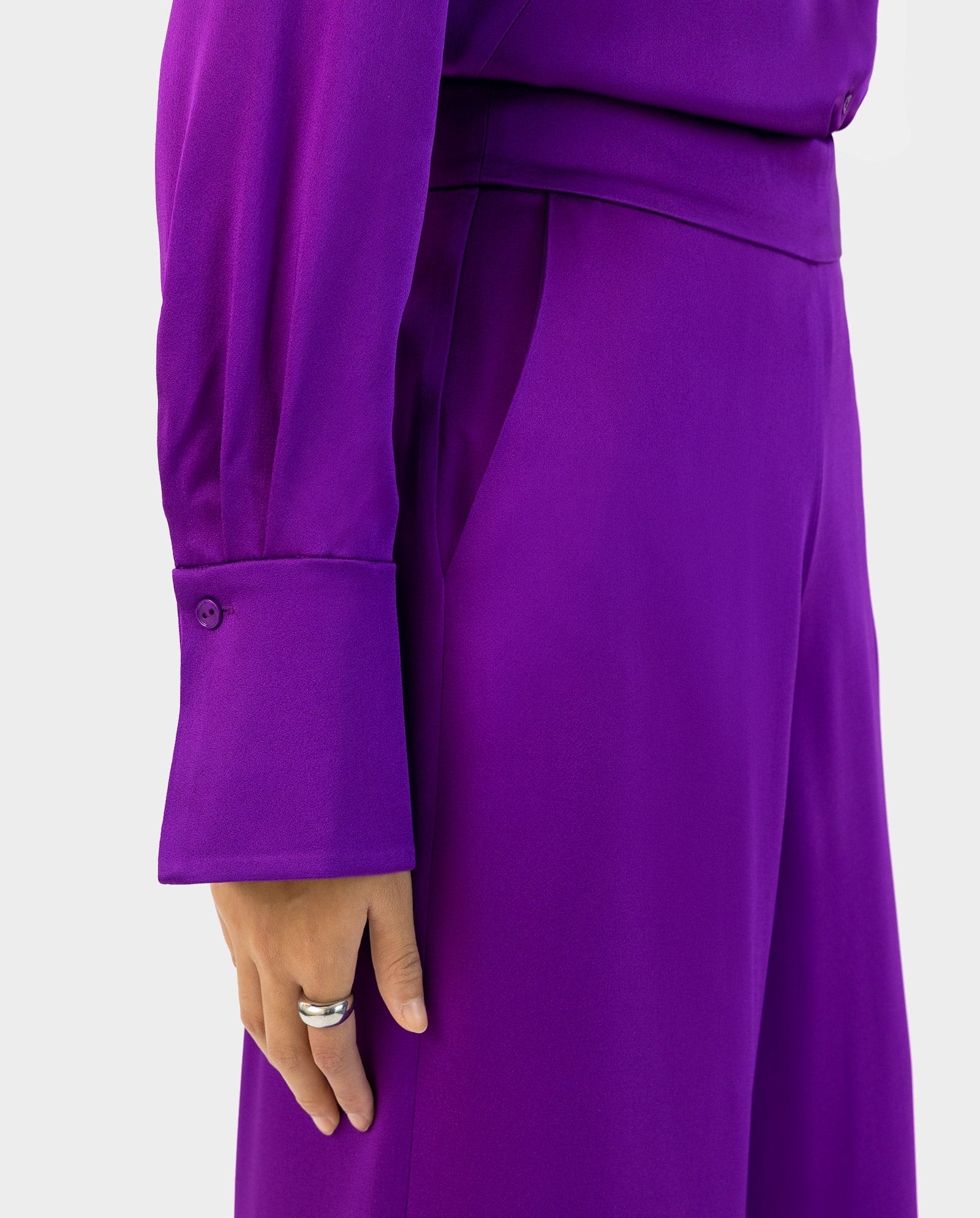 A person showcases their hand while wearing IVY OAKs PETUNIA Trouser, styled with a bright purple long-sleeve top featuring wide cuffs and side pockets for an effortlessly chic look.