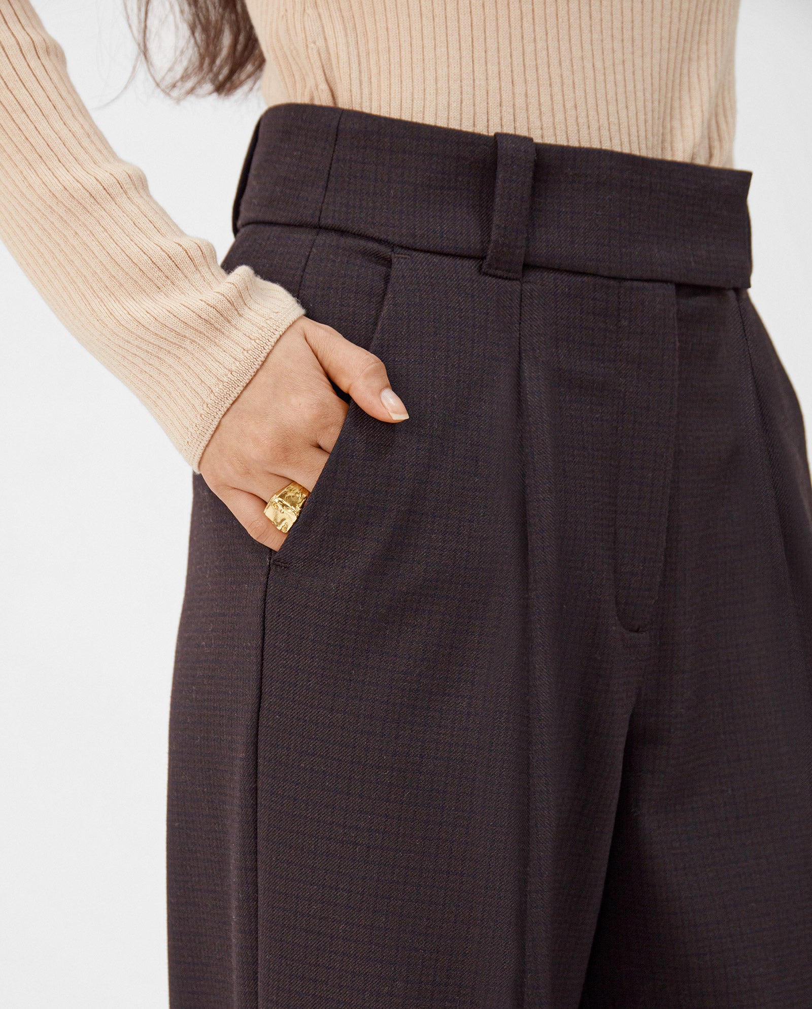 A woman wears IVY OAKs PEONY ROSE Wide Leg Pants in dark tones and a beige ribbed top, with her hand in her pocket displaying a gold ring.