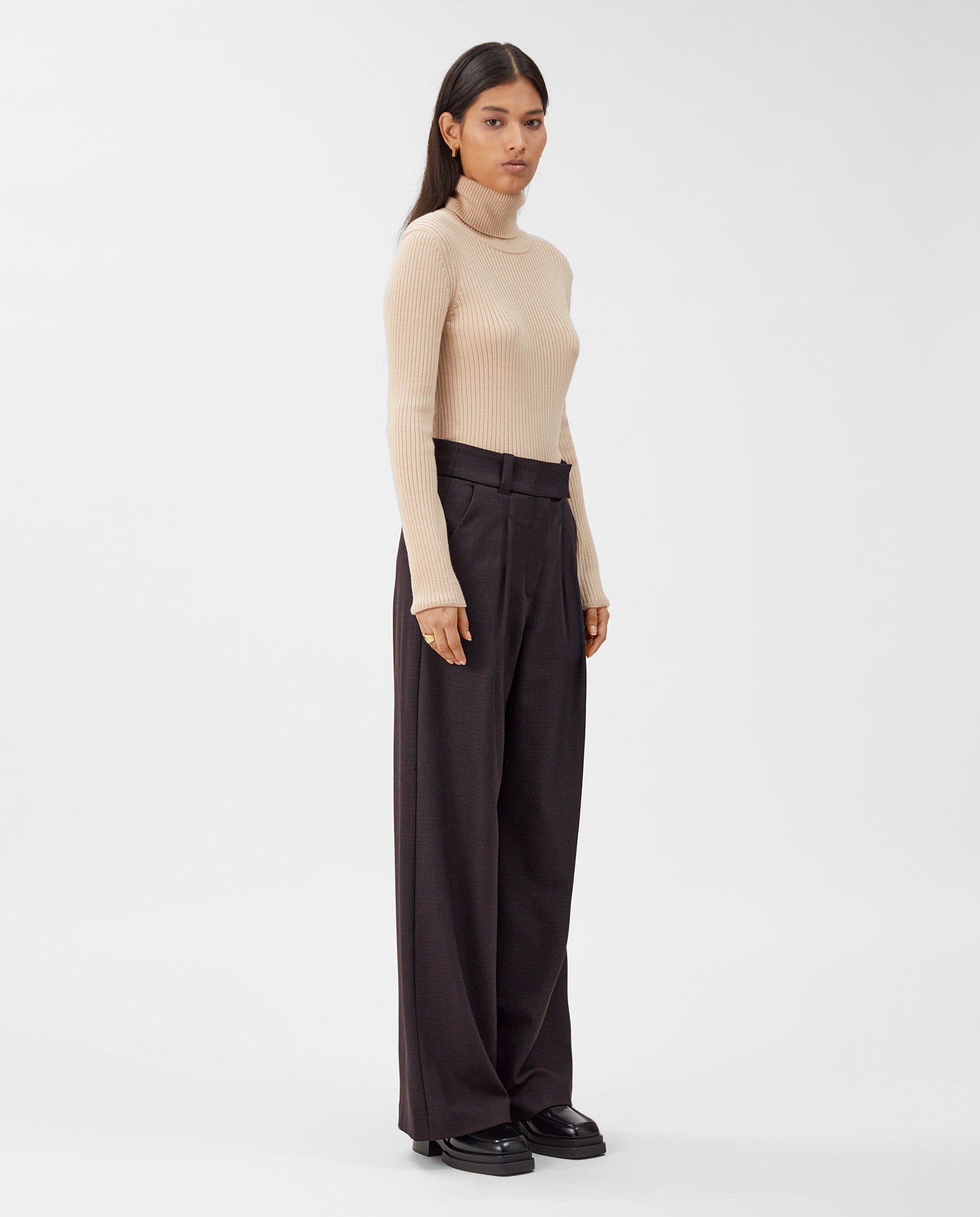 A woman stands against a plain white background wearing IVY OAKs PEONY ROSE Wide Leg Pants and a beige turtleneck sweater.