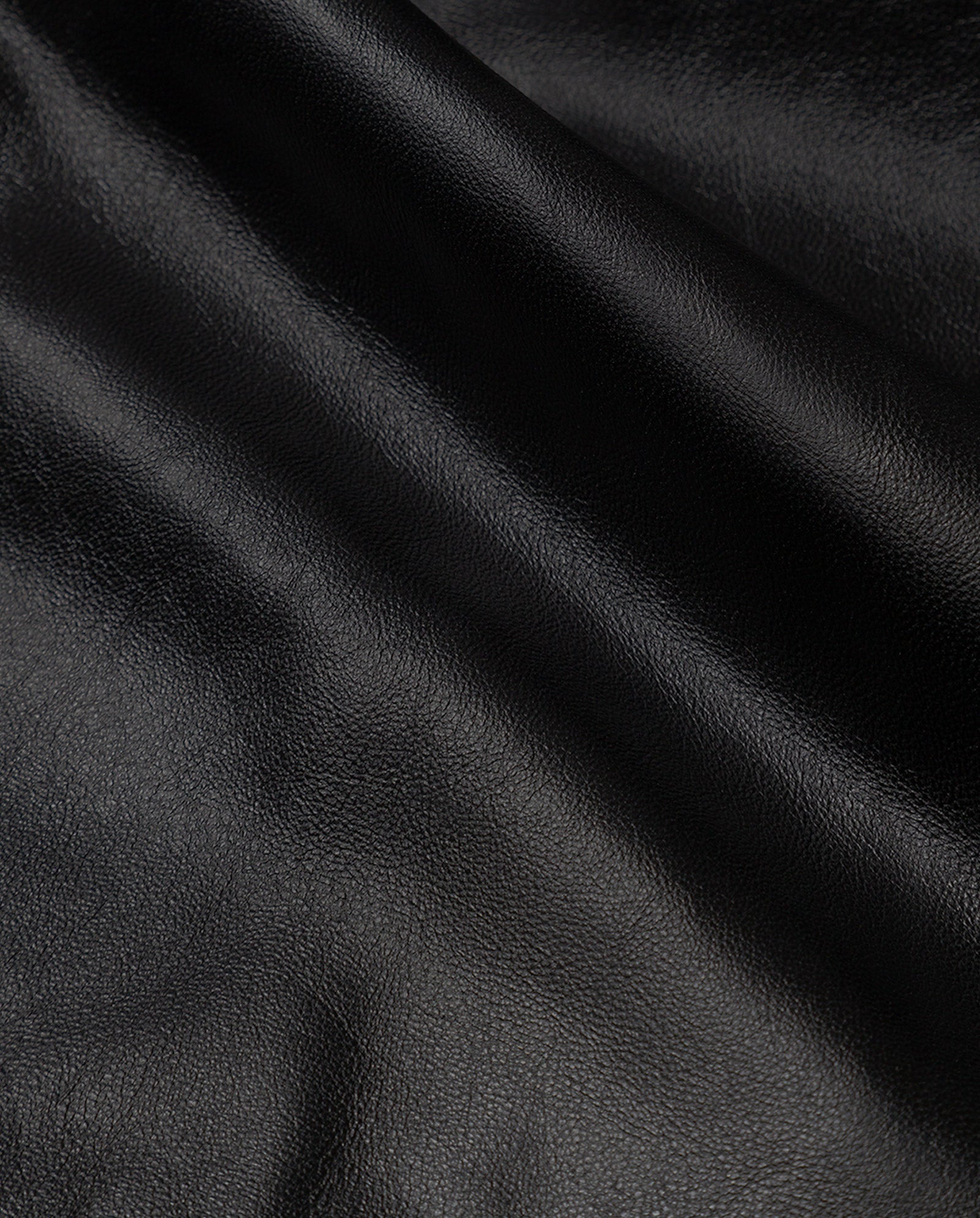 Close-up of smooth black lamb nappa leather with gentle folds and subtle shine, featured in the LIONNE Coat by IVY OAK—a perfect choice for a luxurious trench coat.