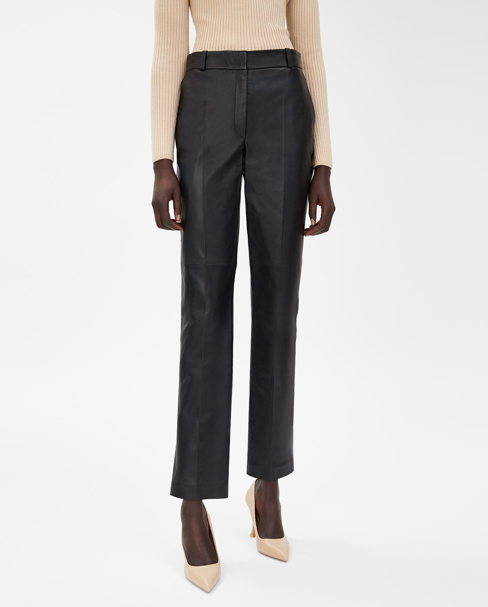 Person wearing IVY OAKs LAURA Pants in black slim fit, a beige ribbed sweater, and nude pointed heels, standing against a white background.