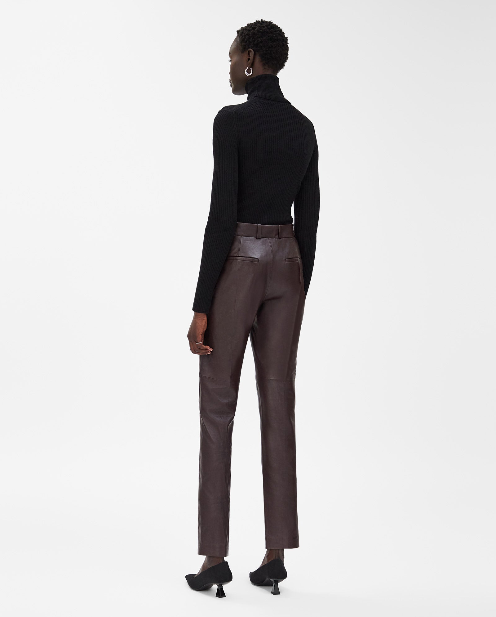 A woman wearing the IVY OAK LAURA Pants, high waist and slim fit in black leather, stands facing away against a white background.