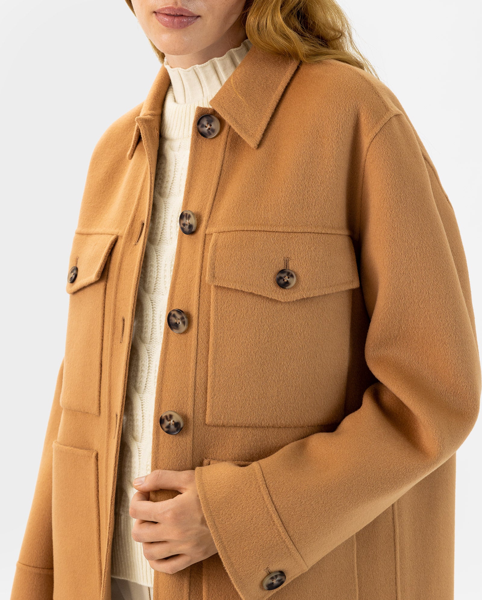 A woman wears the IVY OAK JUNO jacket in camel wool with patched pockets over a cream cable-knit turtleneck, both crafted to meet the Responsible Wool Standard.