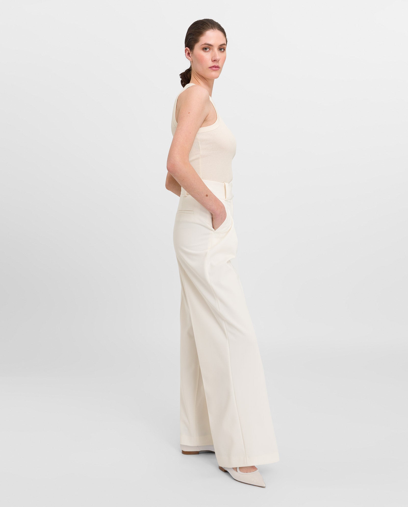 Woman in the IVY OAK KLARA ANN cream organic cotton tanktop with round neck and wide-leg pants, standing sideways with hands in pockets against a white background.