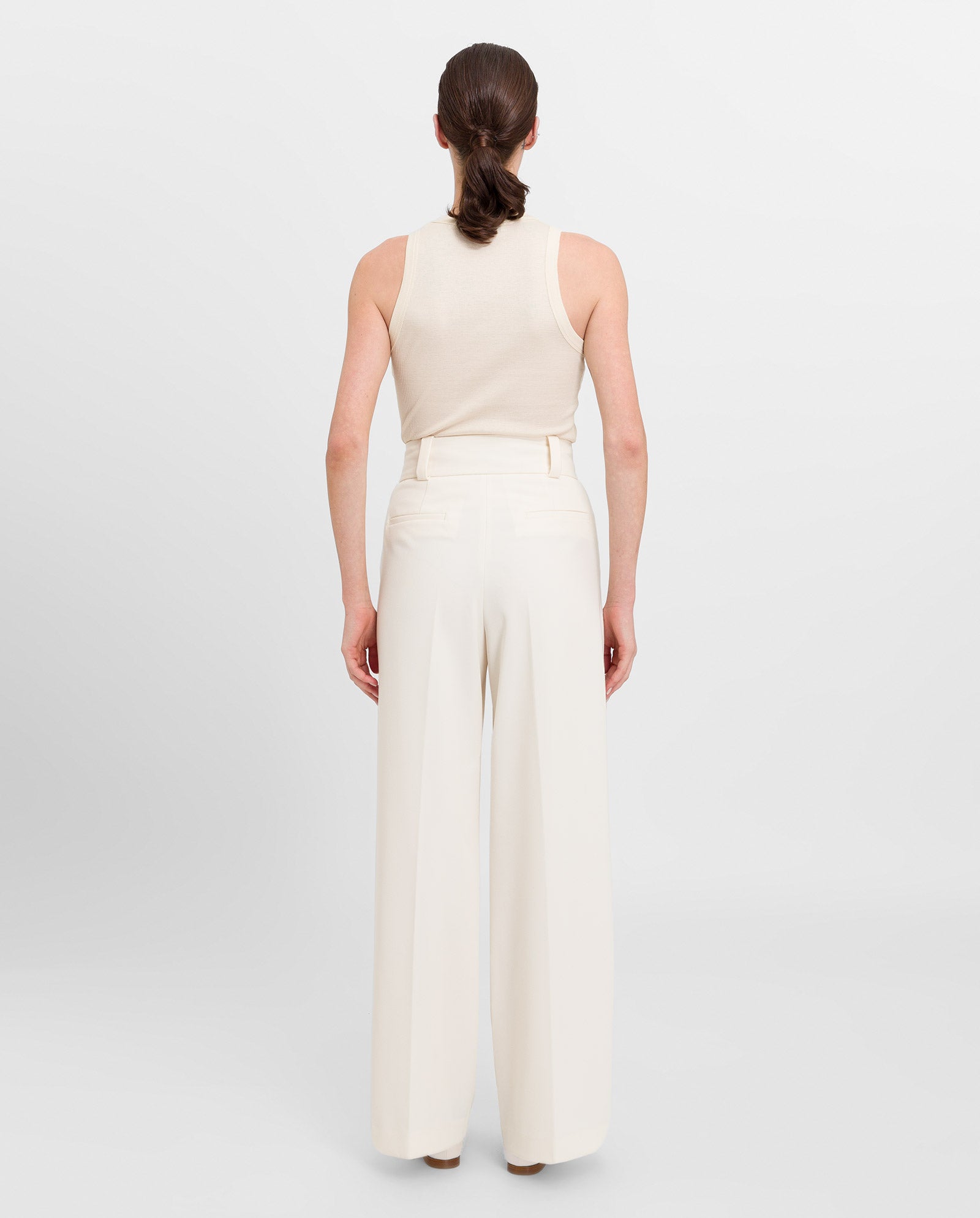 A woman faces away wearing the IVY OAK KLARA ANN sleeveless organic cotton tanktop and high-waisted wide-leg white pants.