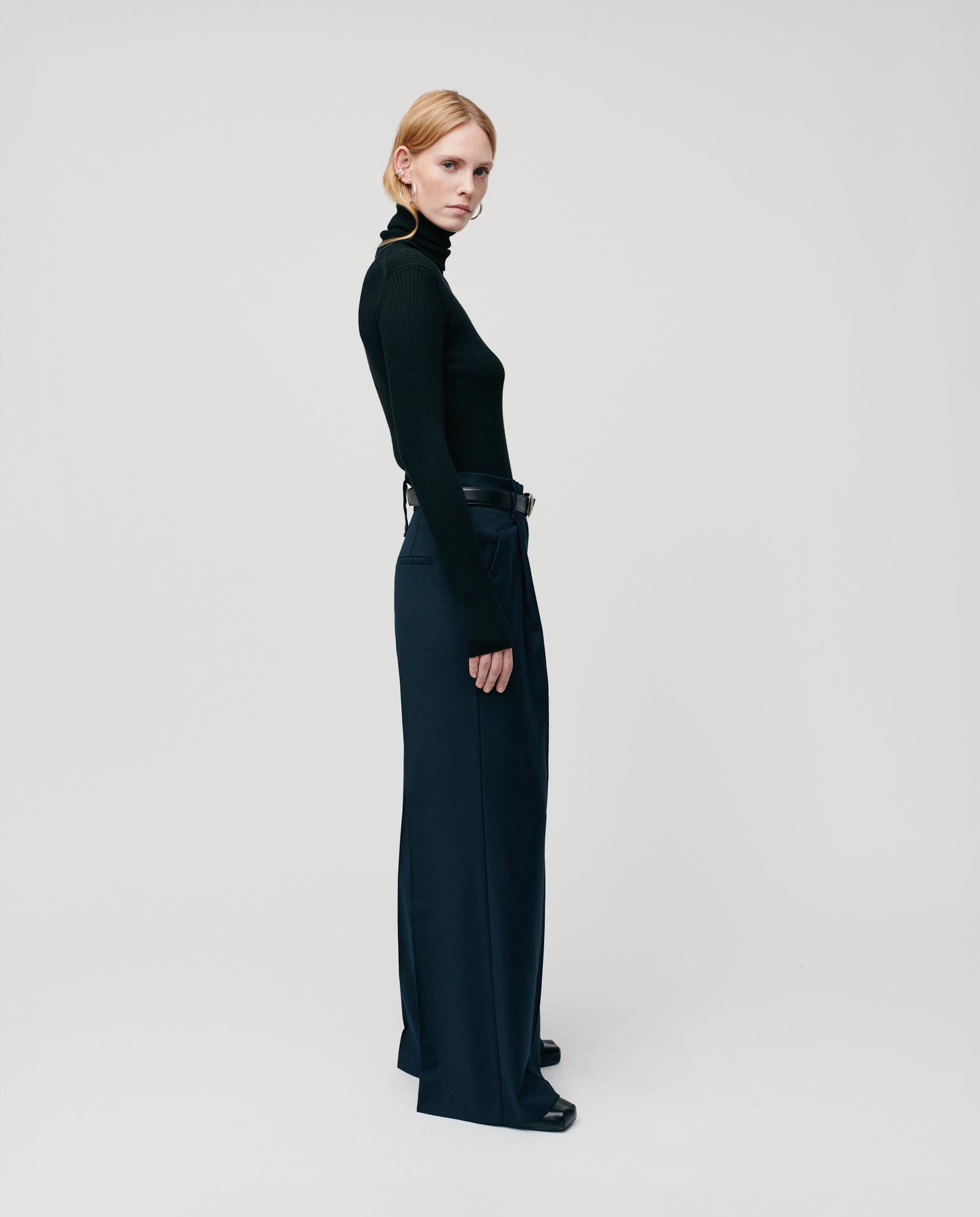 A person with straight blond hair wears the IVY OAK KARO Jumper and navy wide-leg pants, standing sideways.