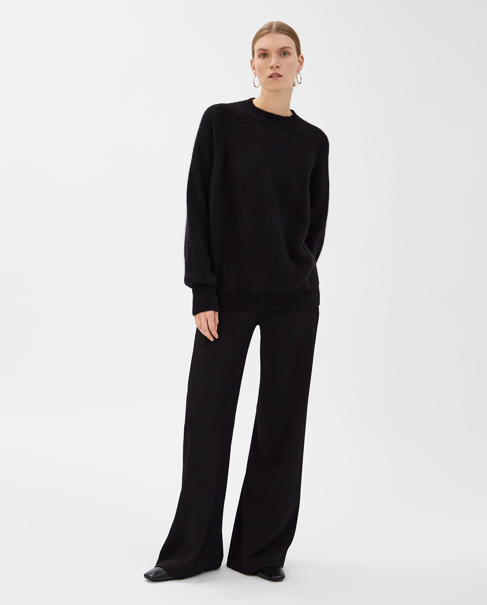 A woman wears the IVY OAK KIRSTEN Jumper in alpaca blend with raglan sleeves and wide-leg black pants, standing against a plain white background.
