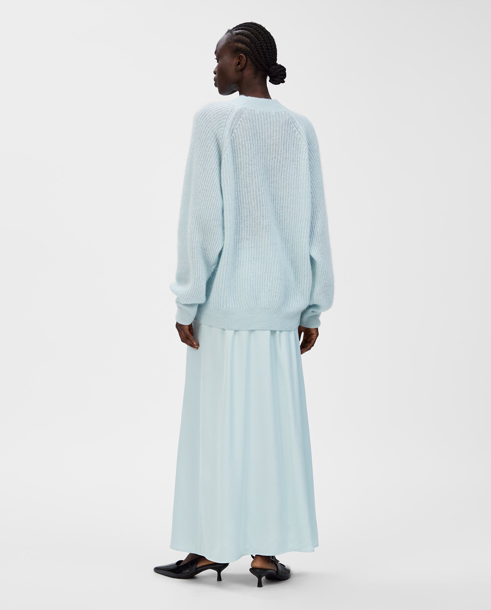 A woman faces away on a plain white background, wearing an IVY OAK KIRSTEN Jumper in light blue with raglan sleeves and a matching skirt.