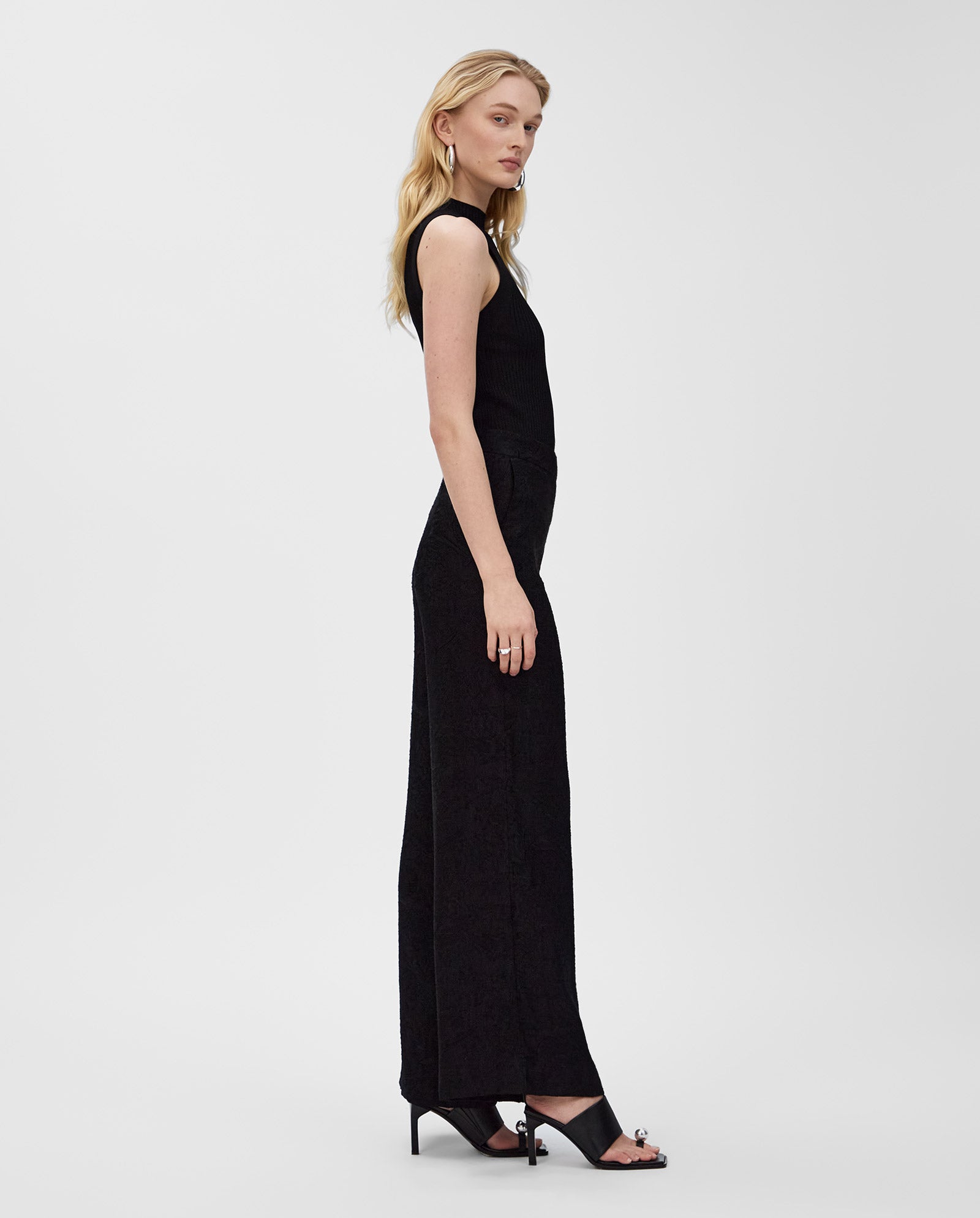 Woman in an IVY OAK KESSIE sleeveless black top and black wide-leg pants with black high heels, standing sideways.