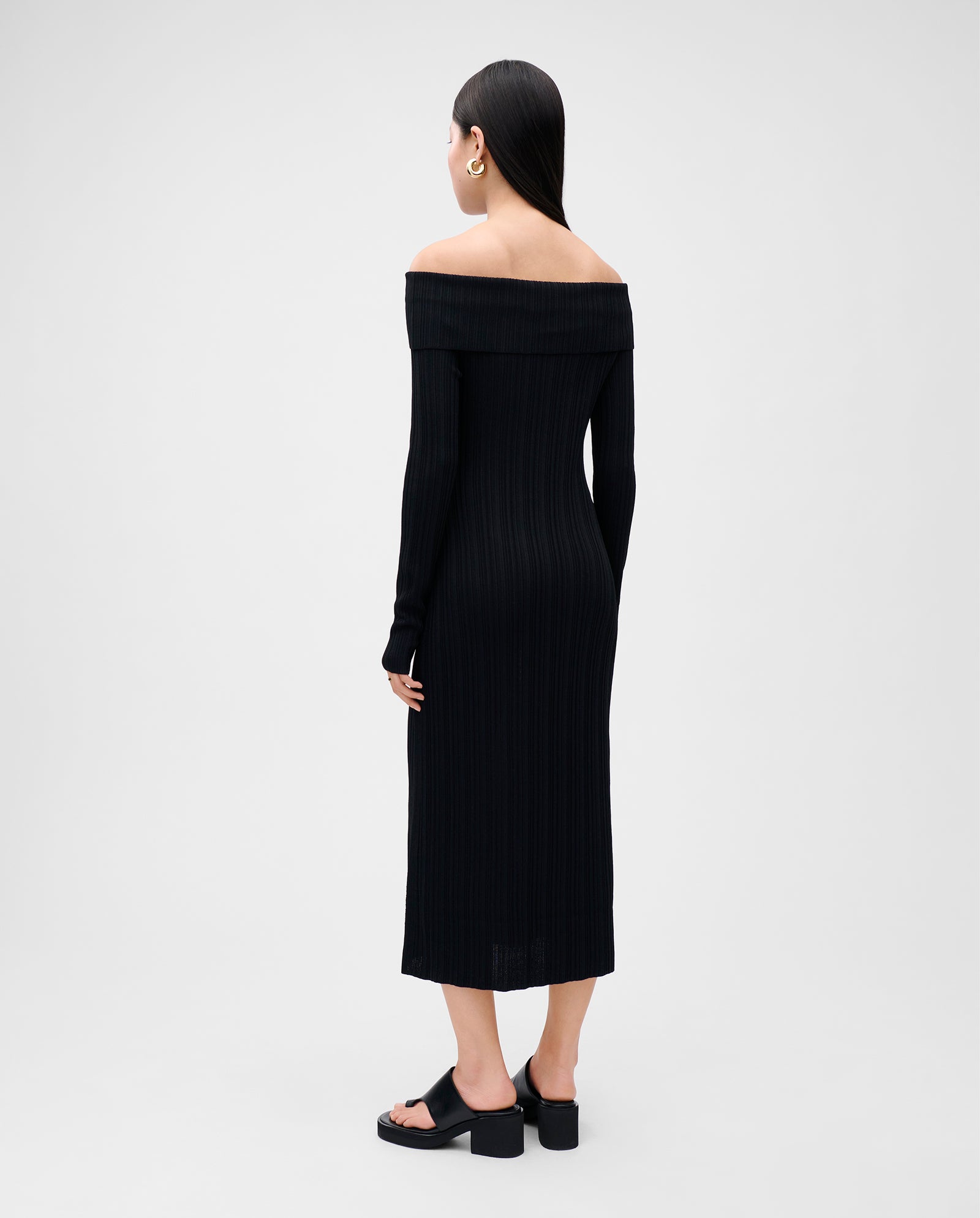 Woman in a figure-hugging IVY OAK KANDICE Dress with a carmen neckline and black sandals, standing with her back to the camera.