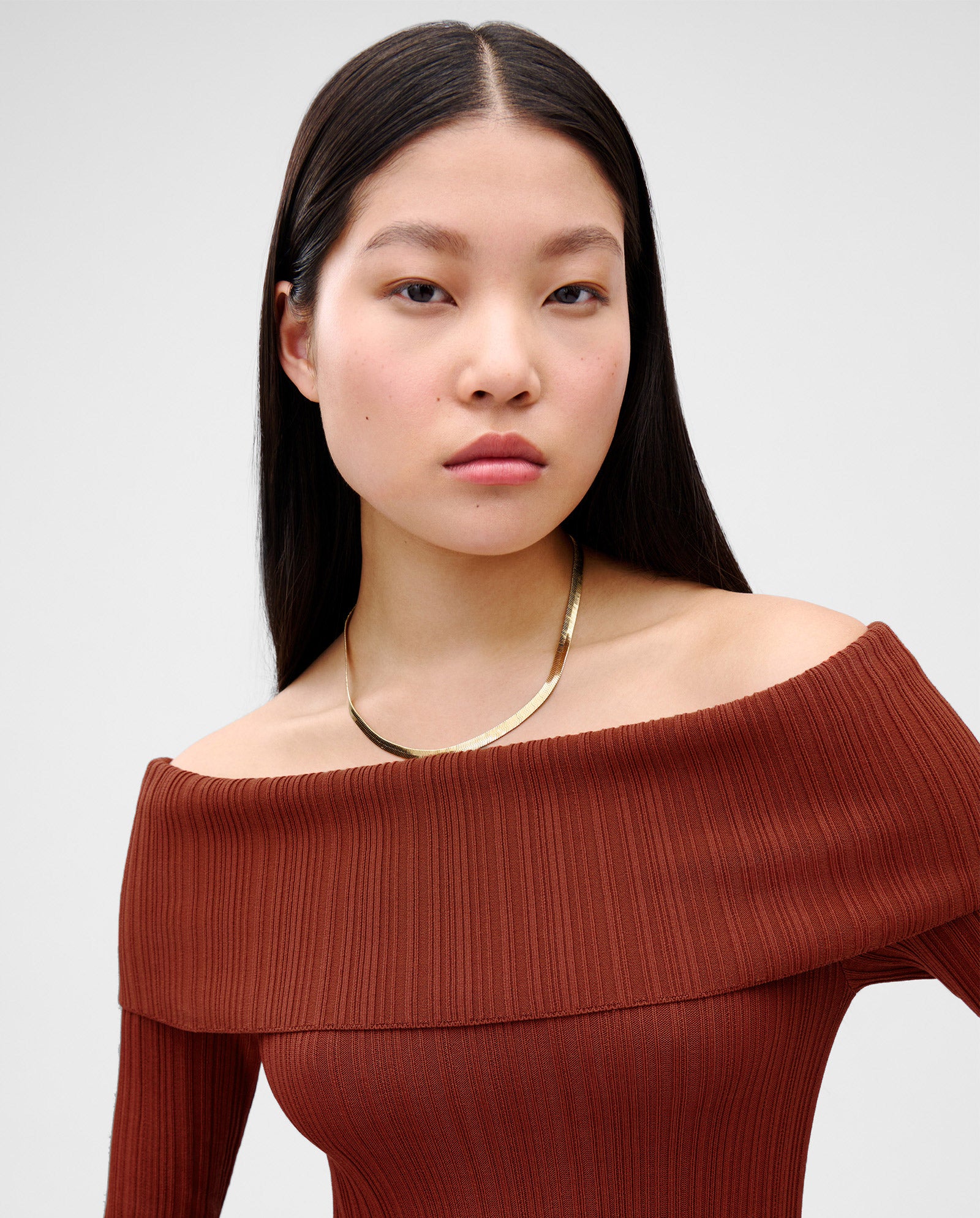 A woman with long straight hair wears the IVY OAK KANDICE Dress, featuring a figure-hugging fit and carmen neckline, paired with a gold necklace, looking at the camera.