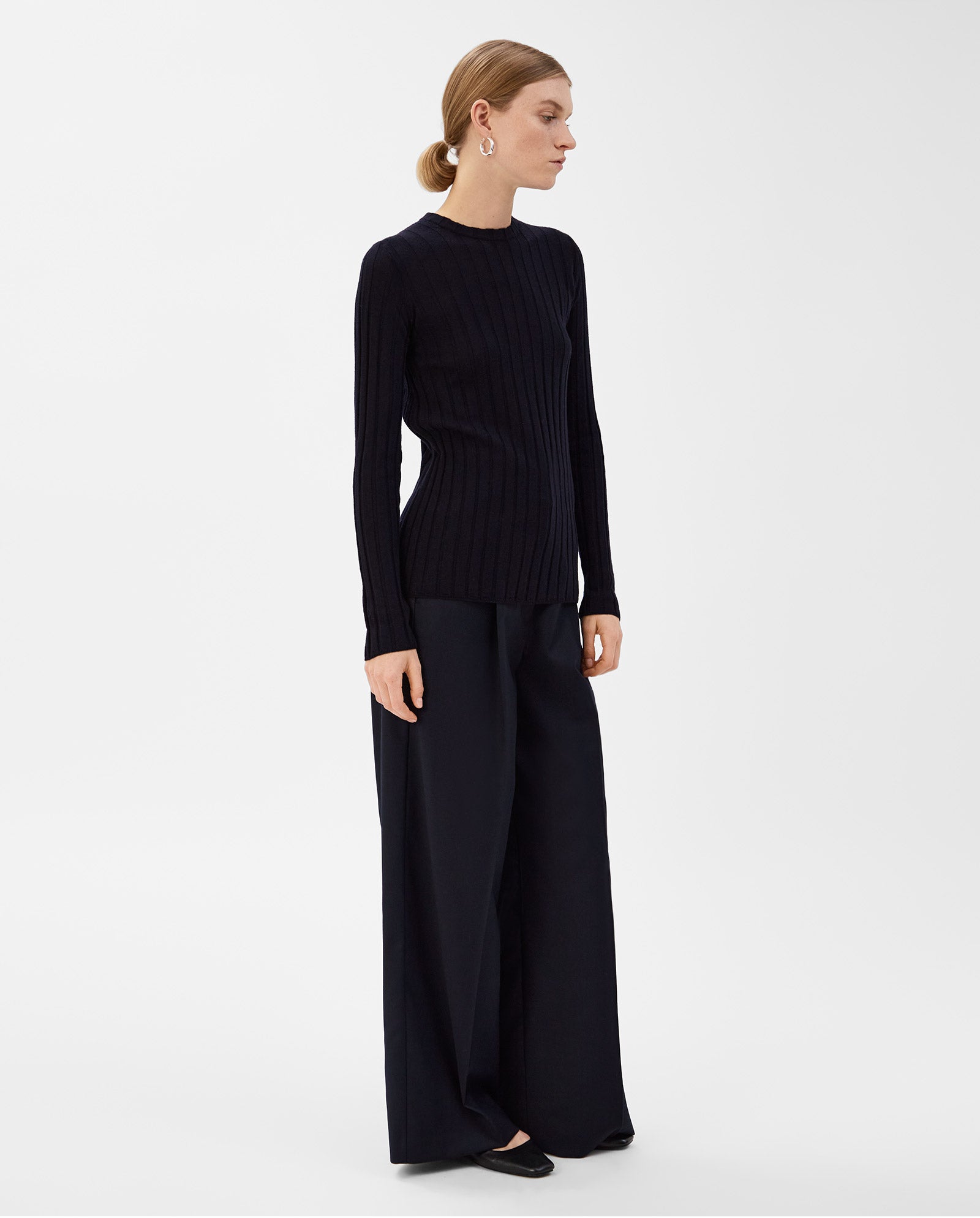 A woman wearing the IVY OAK KACY ANN Top and wide-leg black pants, standing against a plain white background—an ideal look for the transitional season.