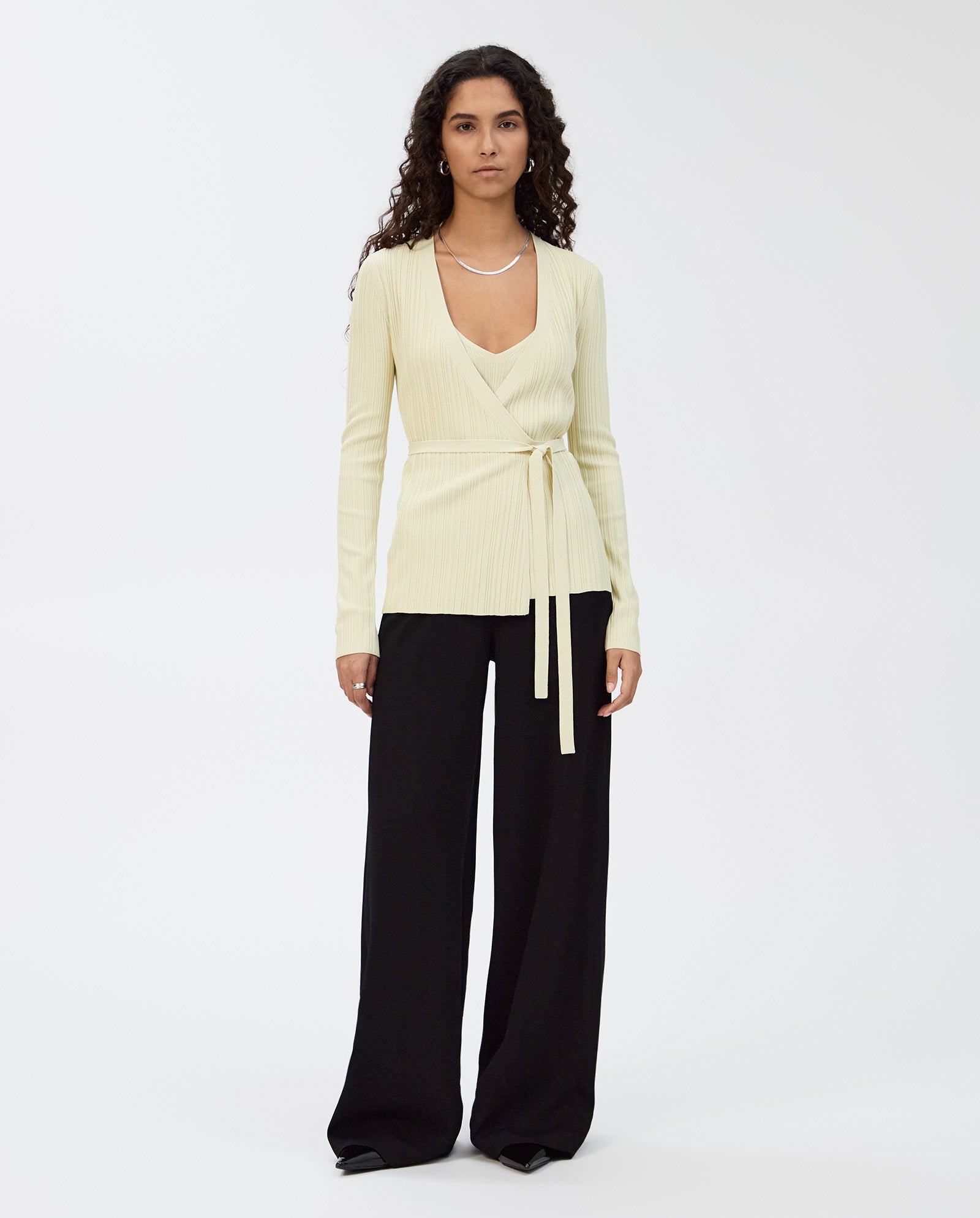 Woman with long curly hair wears the IVY OAK KIERA Cardigan and wide-leg black pants, standing against a white background.