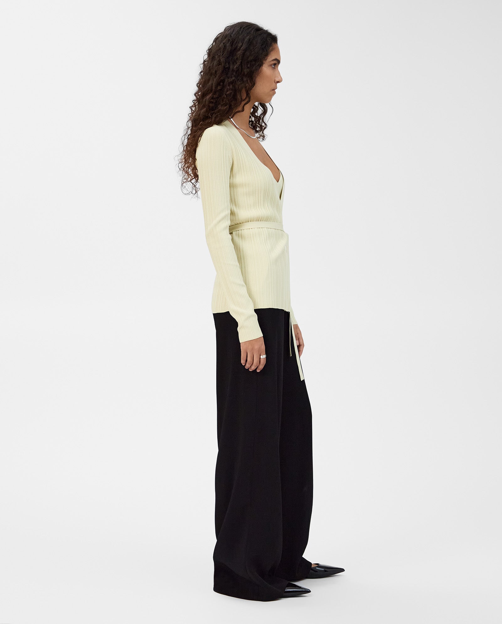 A woman wearing the IVY OAK KIERA Cardigan and loose black pants stands in profile against a plain white background.