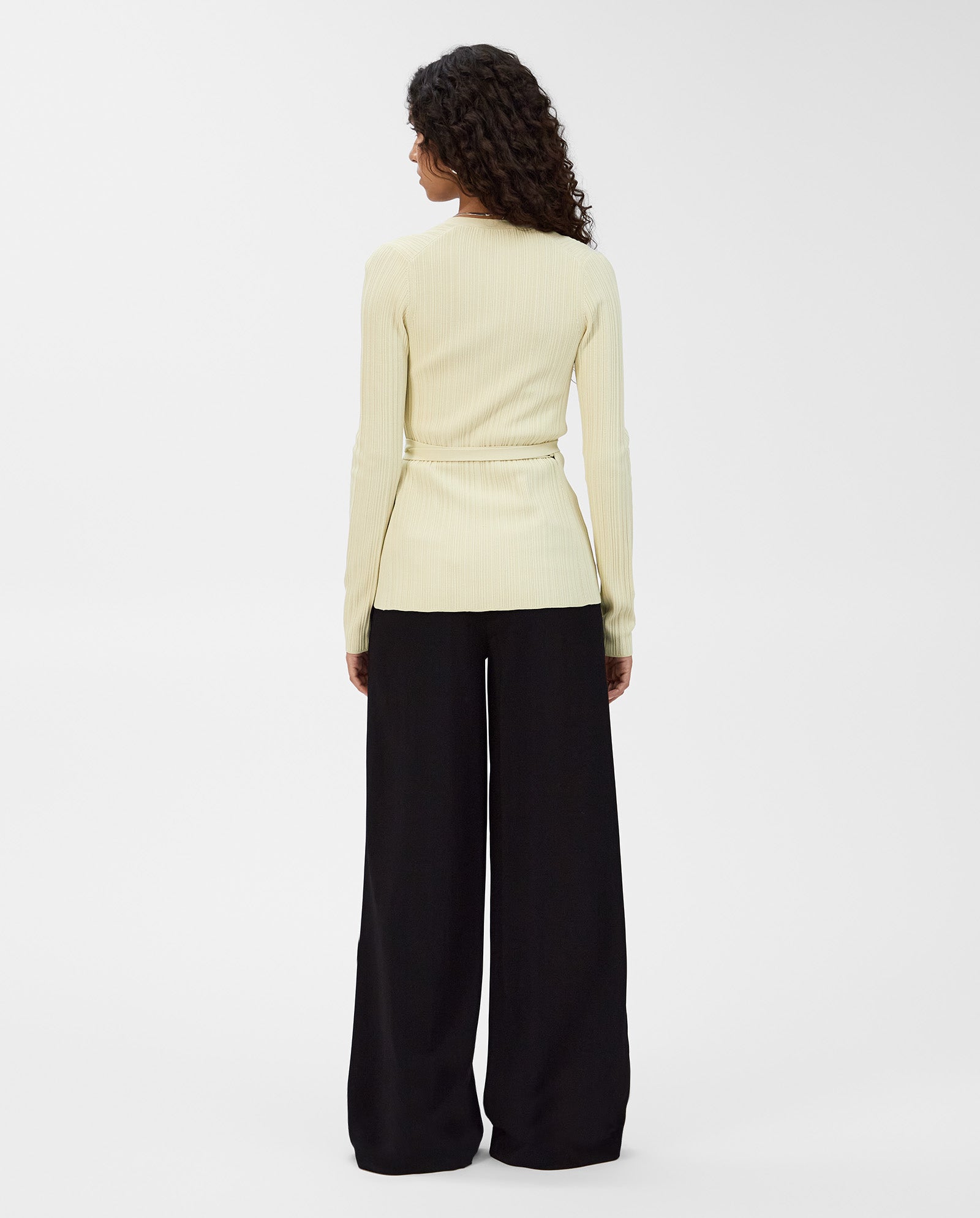 A person with curly hair is shown from the back wearing the IVY OAK KIERA Cardigan with elegant sleeves, paired with wide-leg black pants.