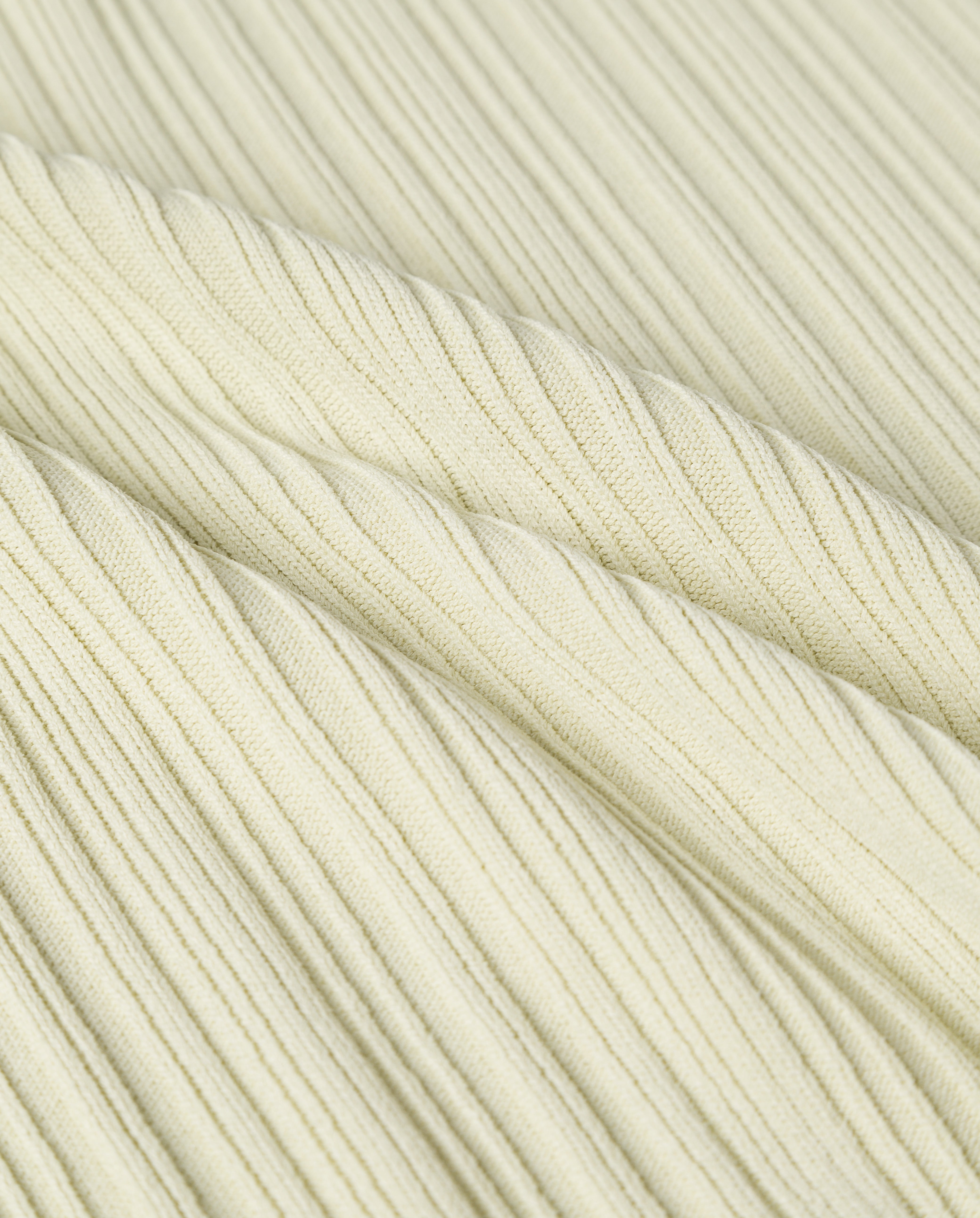 Close-up of the KIERA Cardigan by IVY OAK shows light yellow ribbed fabric with soft, diagonal folds and an irregular knit structure, highlighting its elegant texture.