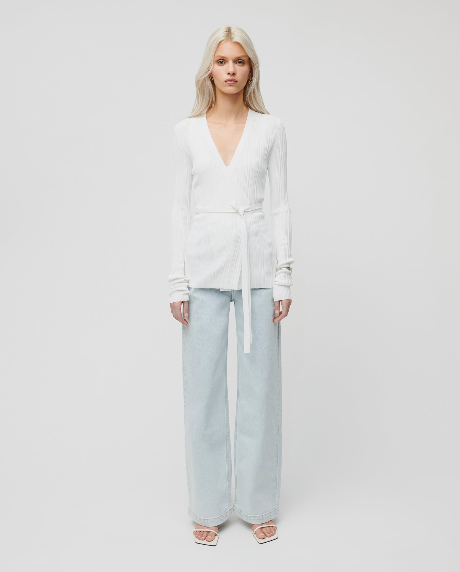 A woman wears the IVY OAK KIERA Cardigan with elegant sleeves and light blue wide-leg jeans, standing against a plain white background.