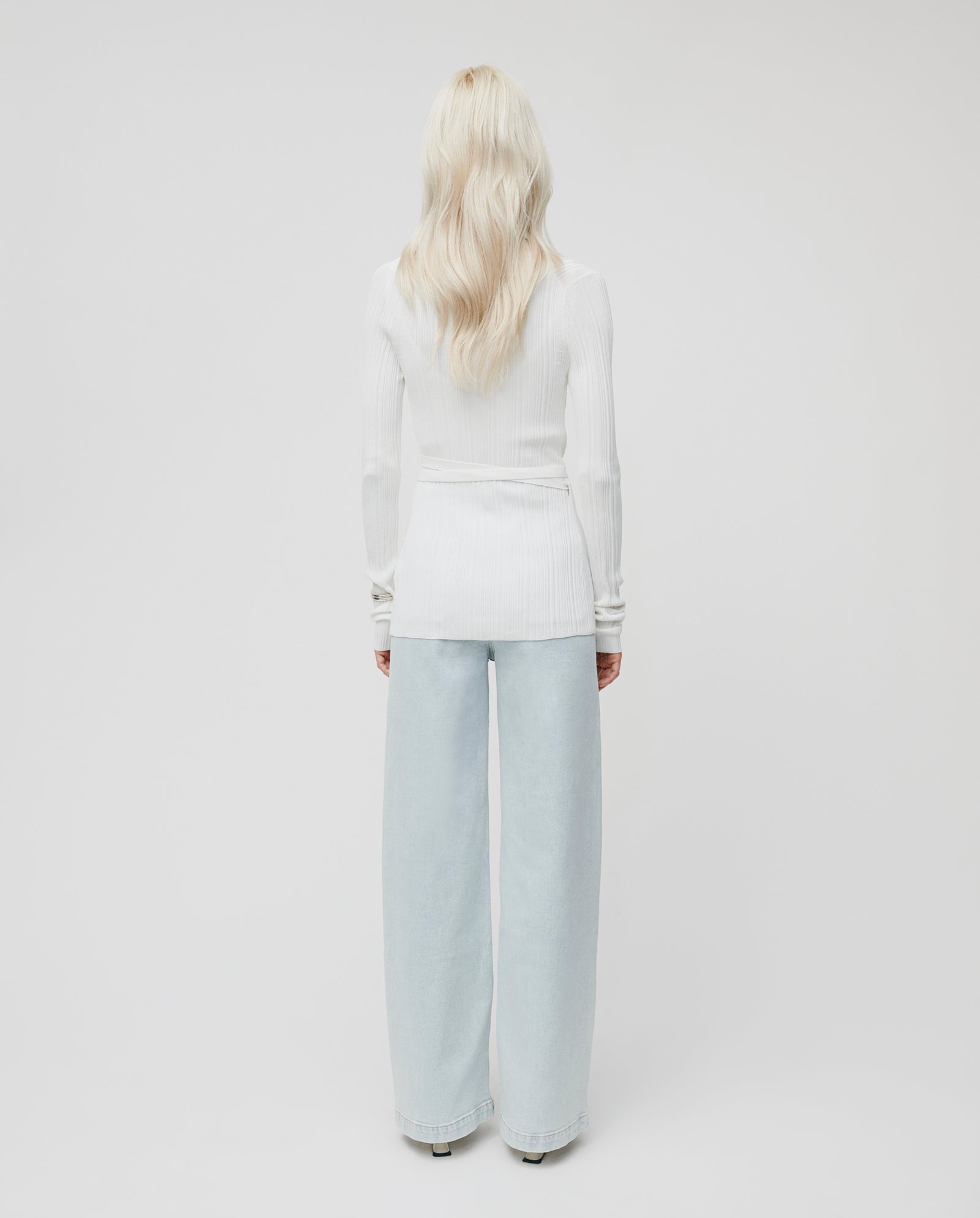 A person with long blonde hair is shown from the back, wearing the IVY OAK KIERA Cardigan with elegant sleeves and light blue wide-leg jeans.