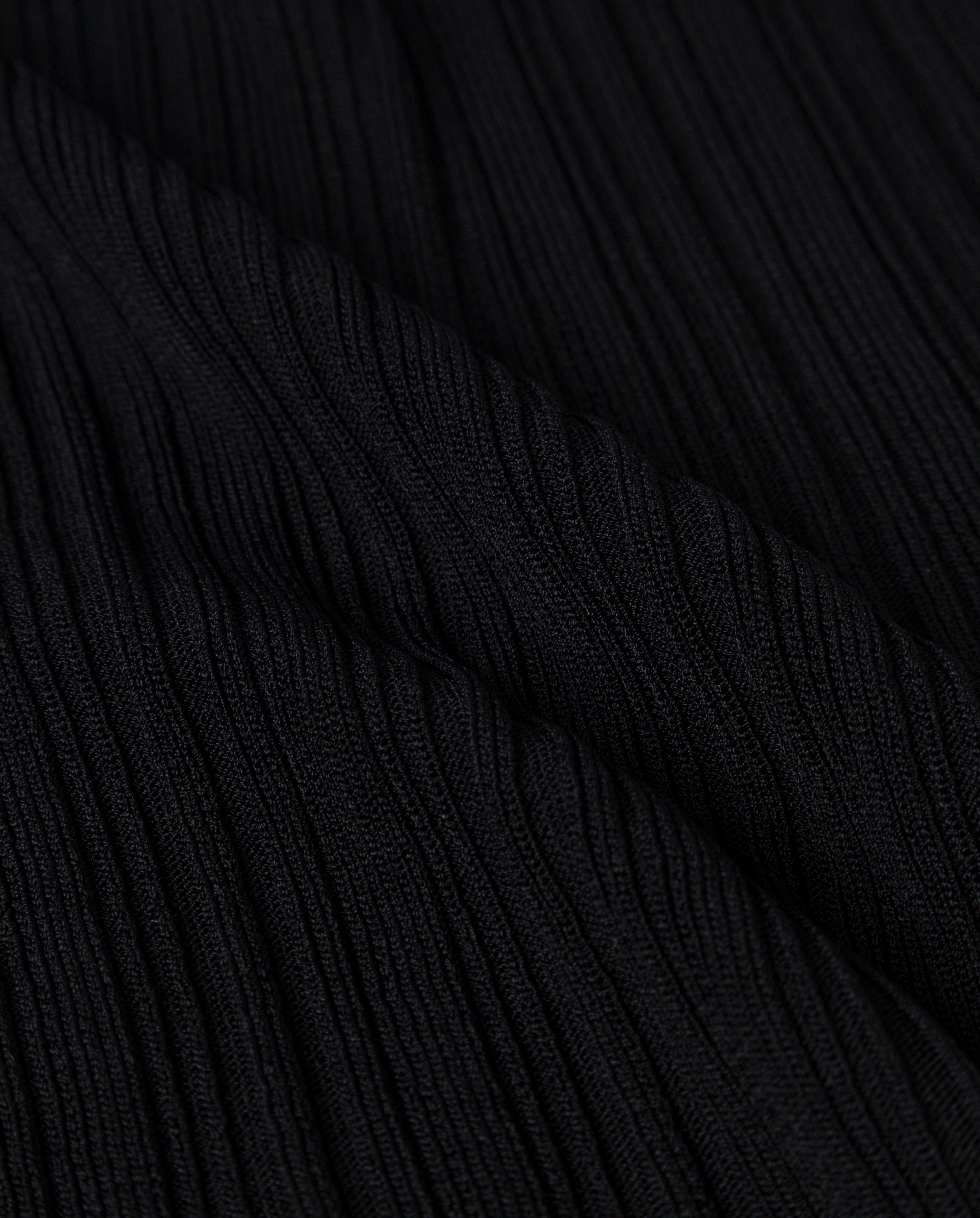 Close-up of black ribbed fabric with textured vertical lines and folds, featured on the KLOE Dress by IVY OAK.