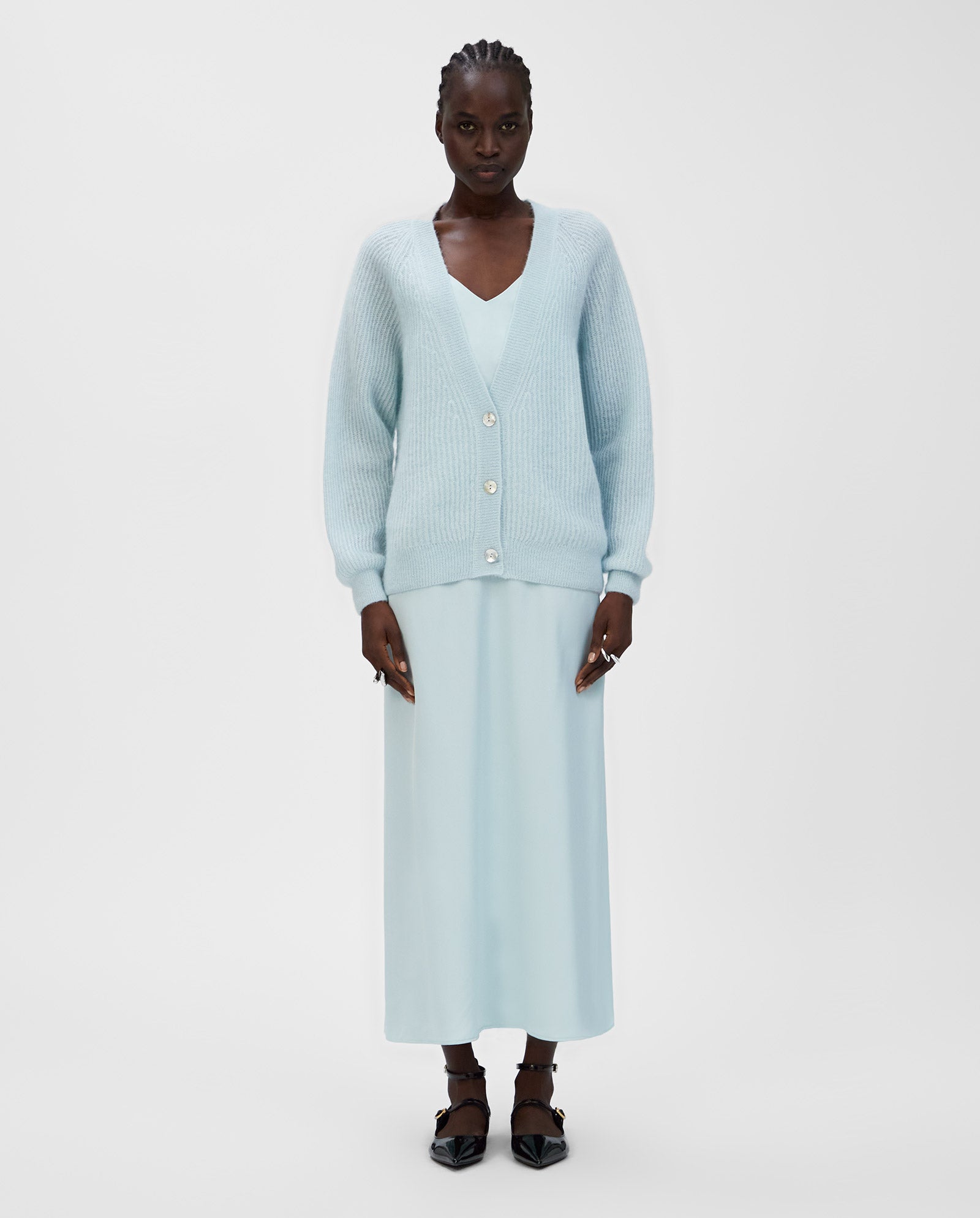 A woman wears the KEONA ANN Cardigan by IVY OAK, an alpaca blend light blue cardigan with a deep neckline and a matching long dress, standing against a plain white background.