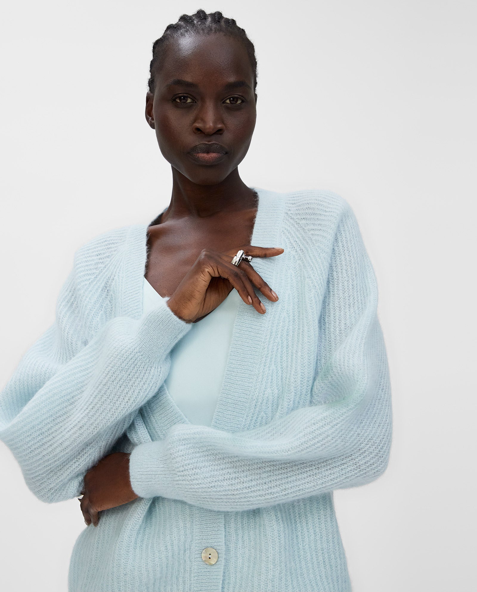 A woman confidently looks at the camera with her arms crossed, wearing the KEONA ANN Cardigan by IVY OAK in light blue alpaca blend.