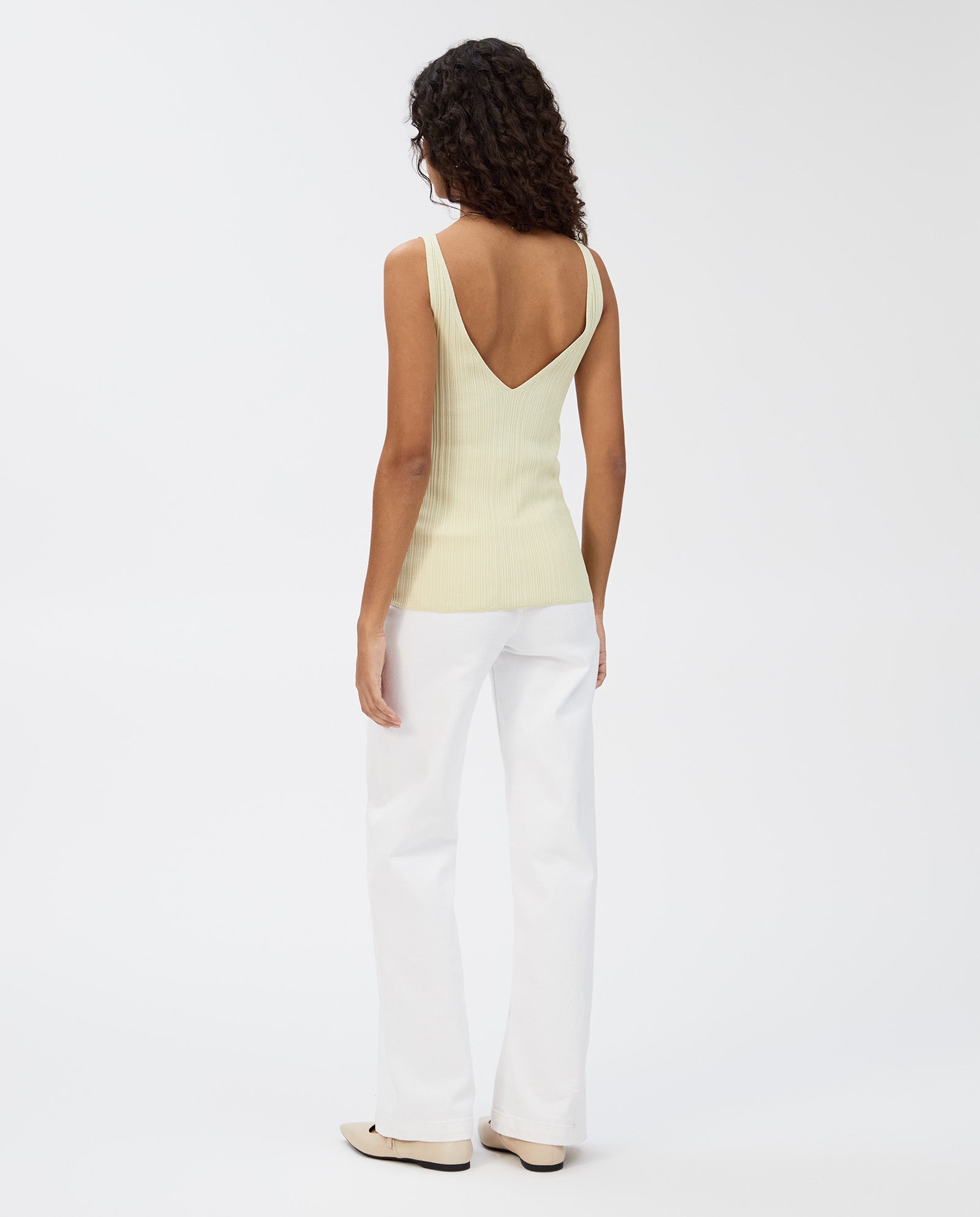 A person wearing the IVY OAK KYM Top in yellow, styled with white pants and beige shoes, stands against a white background.