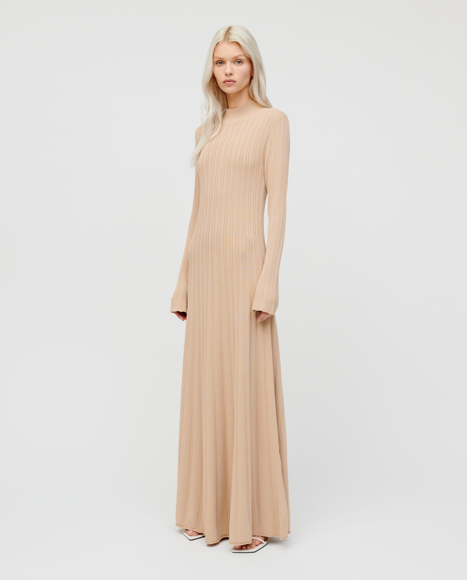 A woman wears the IVY OAK KOURTNEY dress, a long beige viscose knit with a body-hugging fit and long sleeves, standing against a plain white background.