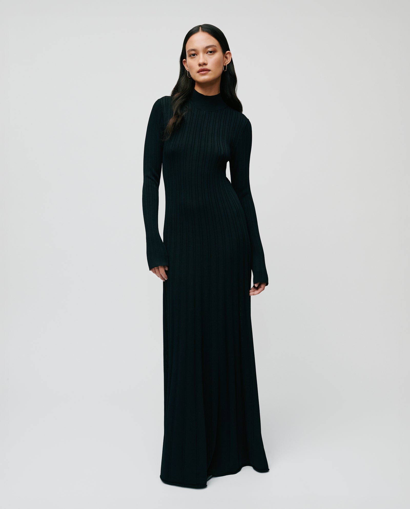 A woman wears the IVY OAK KOURTNEY Dress, a long-sleeved, black viscose knit piece with a body-hugging fit, standing against a plain white background.