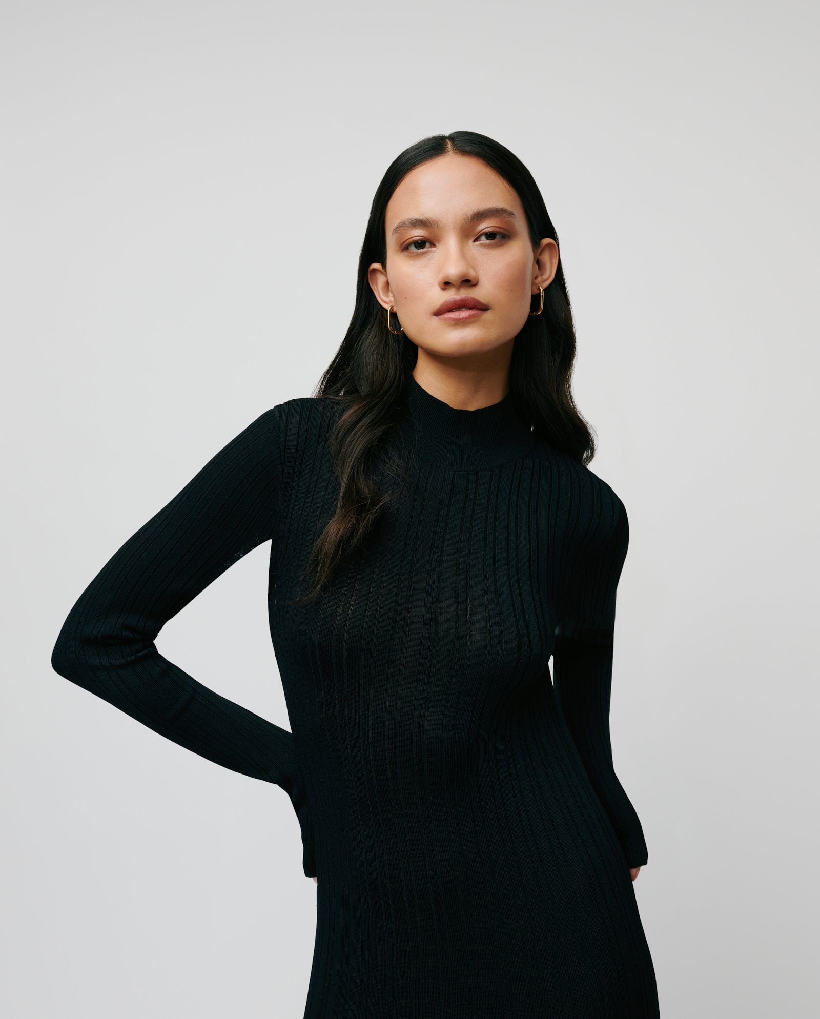 A woman with long dark hair models the IVY OAK KOURTNEY Dress, a viscose knit piece with a body-hugging fit and subtle pleats, set against a plain light background.