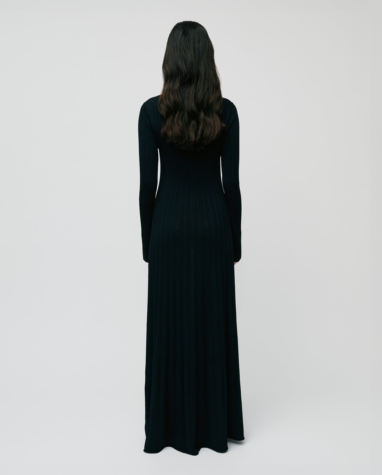 A person with long dark hair, facing away from the camera, wears the IVY OAK KOURTNEY Dress—a black, floor-length viscose knit dress with a body-hugging fit.