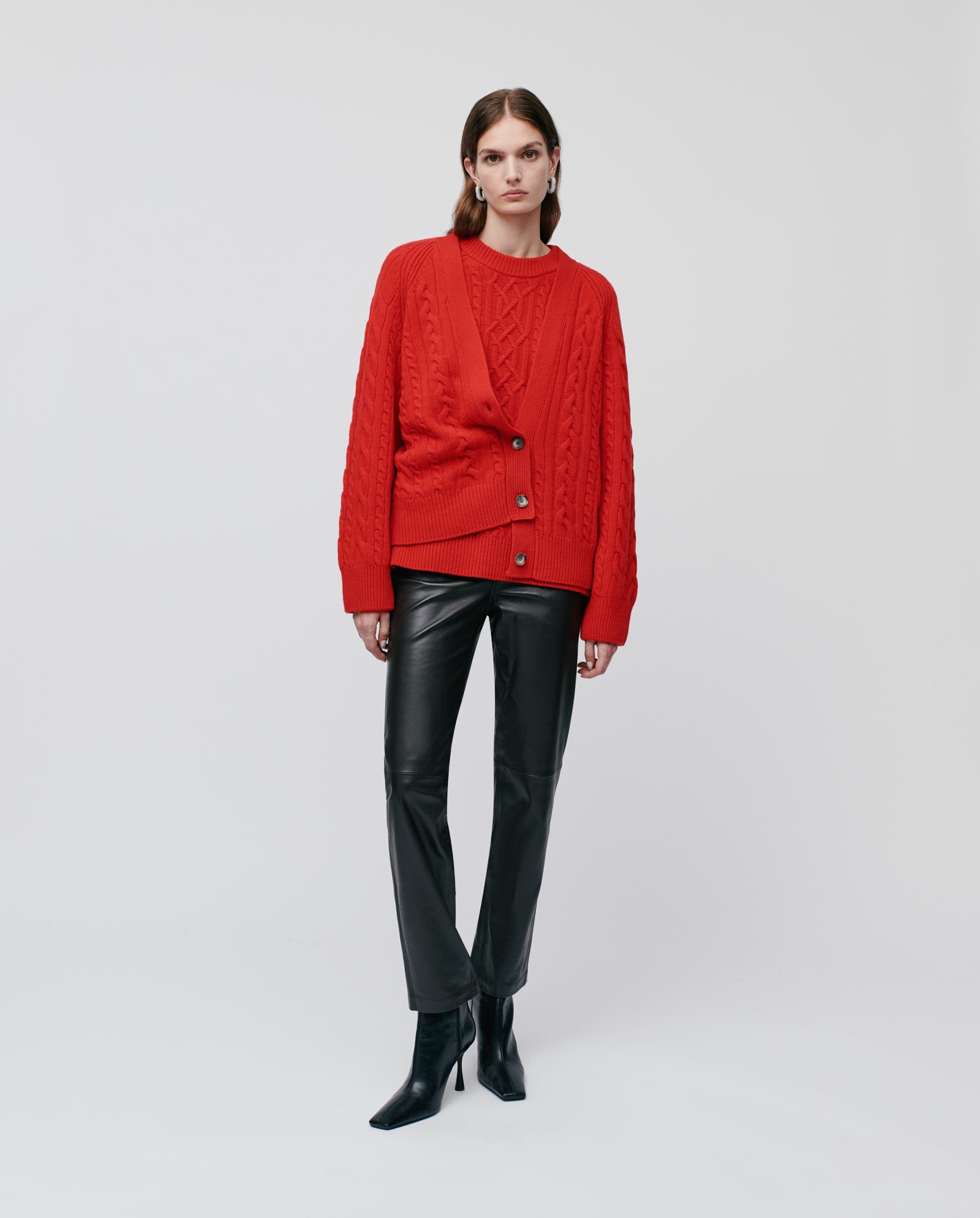 Woman in the IVY OAK KYMBERLY Cardigan, a red cable-knit sweater with a relaxed silhouette, styled with black leather pants and black heeled boots, standing against a white background.