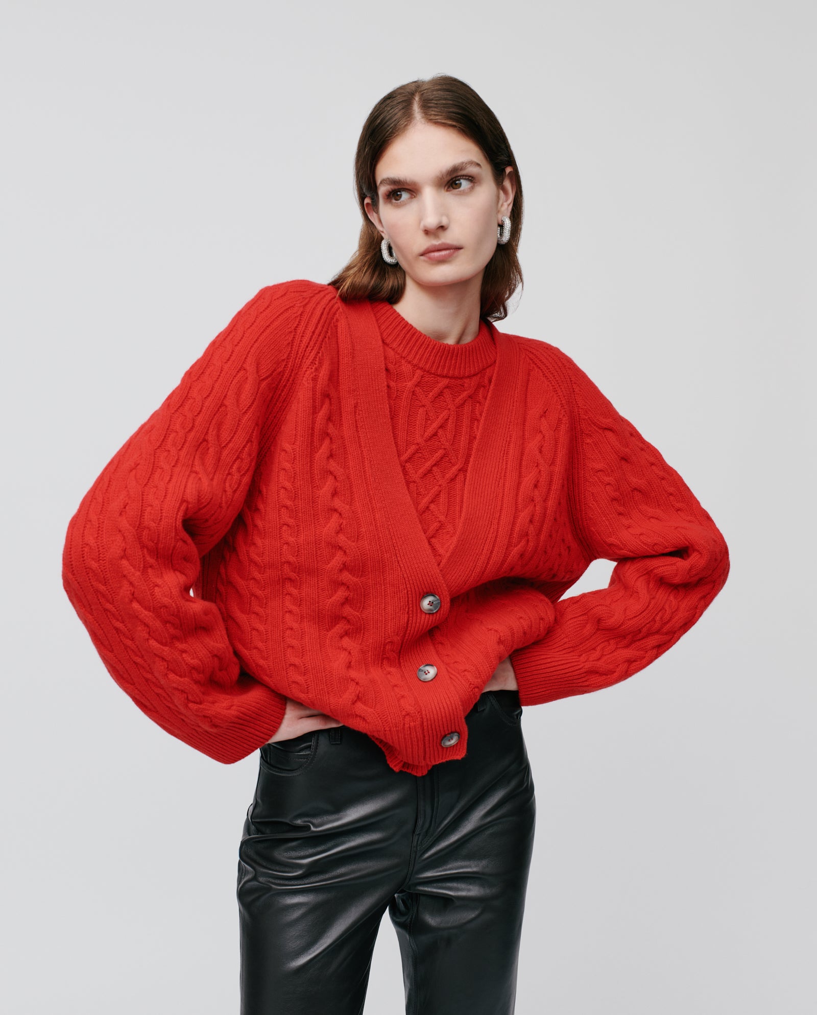 A woman wears the IVY OAK KYMBERLY Cardigan, a bright red chunky knit sweater with a relaxed silhouette, paired with black leather pants against a plain background.