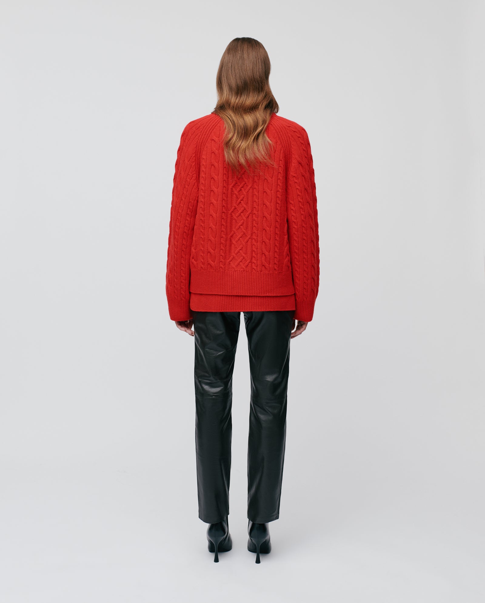 Woman wearing the KYMBERLY Cardigan by IVY OAK, paired with black leather pants and heels, standing with her back to the camera.