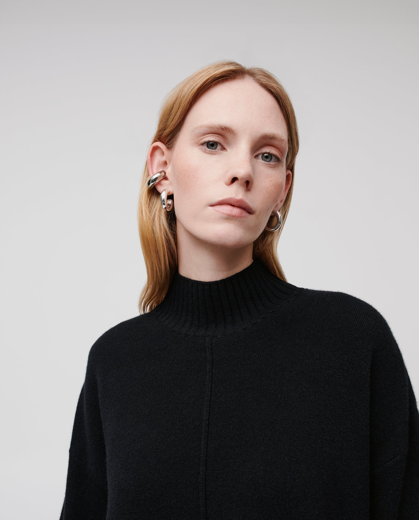 A woman with light hair wears the black KAREEN ROSE Jumper by IVY OAK and silver hoop earrings, pictured against a plain background.