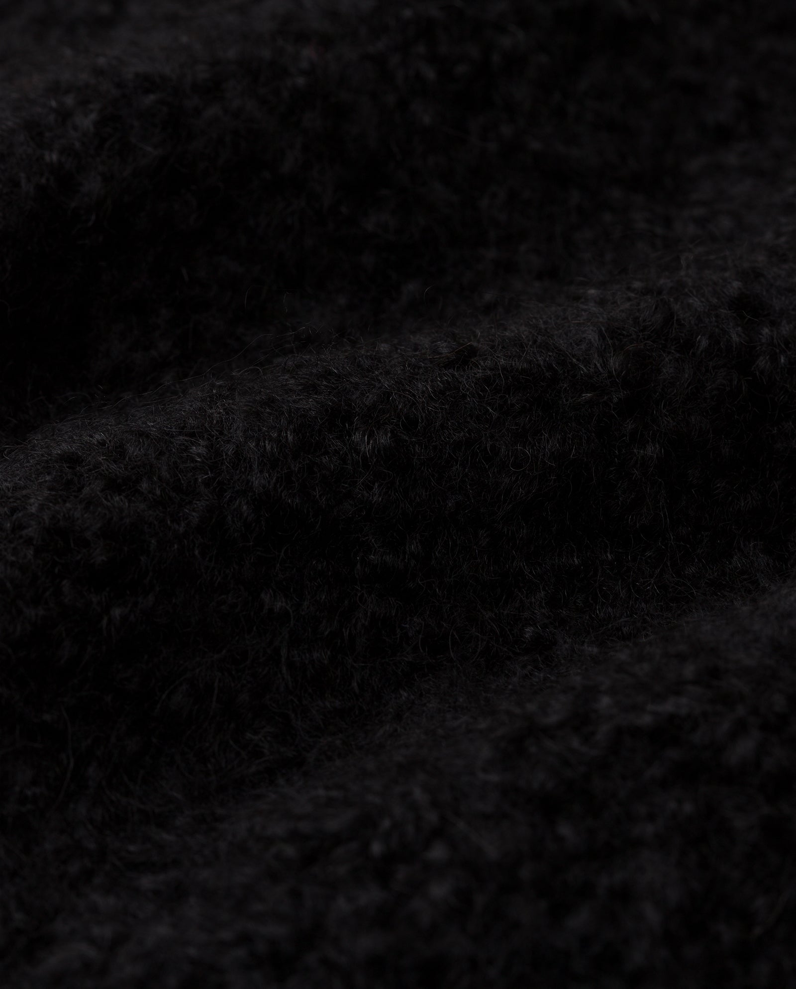 Close-up of the KRISTAL Cardigan by IVY OAK, featuring black, ultra-soft bouclé yarn with a textured, fuzzy finish and a wavy surface pattern.