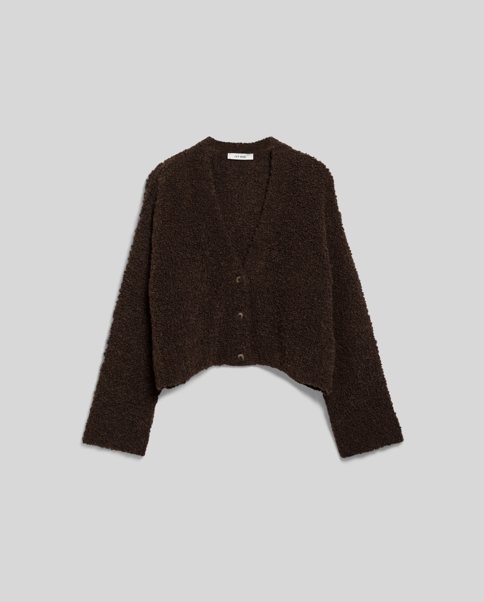 The IVY OAK KRISTAL Cardigan is a dark brown, ultra soft bouclé V-neck with long sleeves and buttons, featuring textured fuzzy fabric, shown laid flat on a gray background for a modern, casual style.