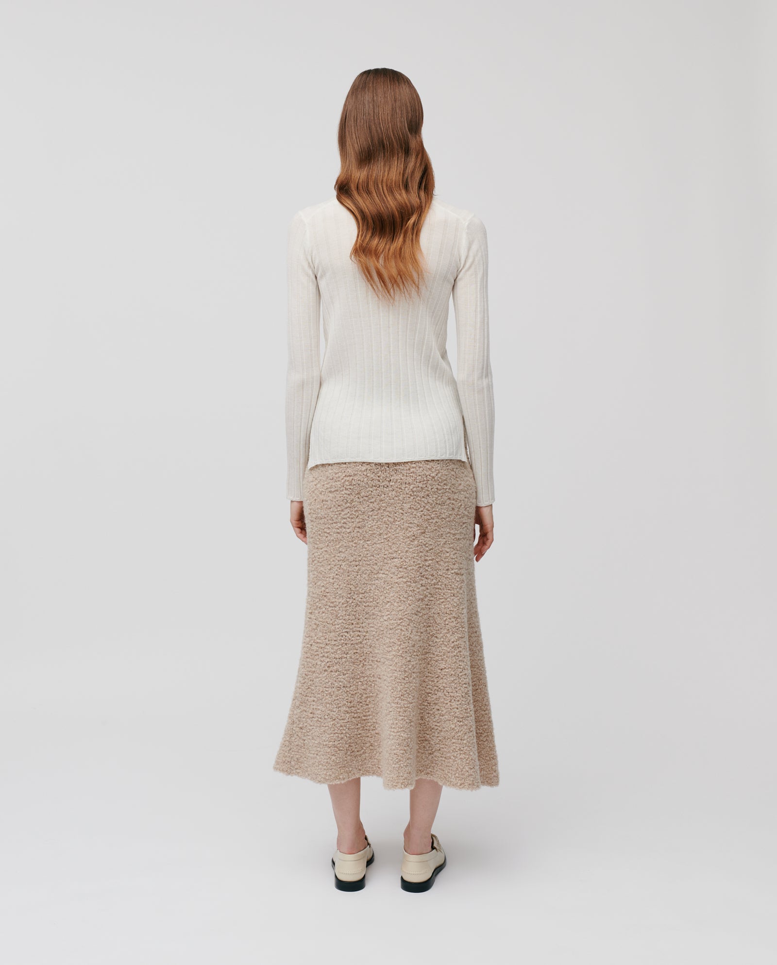 A woman with wavy brown hair, wearing a white sweater and the IVY OAK KRISTYN Skirt—an A-line skirt with an elastic waistband—stands facing away against a white background.