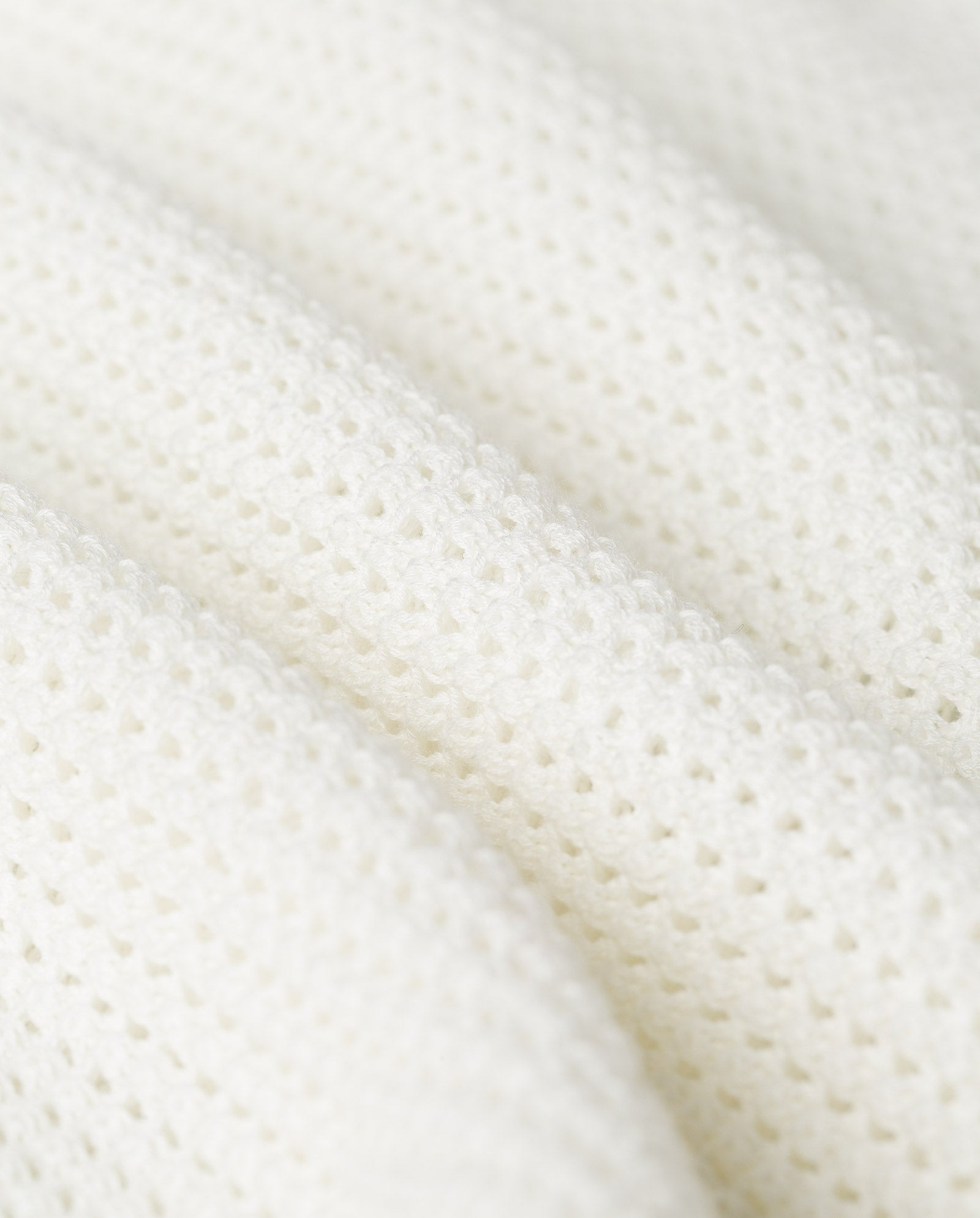 Close-up of the FLO Top by IVY OAK: white textured fabric with small, evenly spaced holes and soft folds, reminiscent of a summer open knit polo shirt.