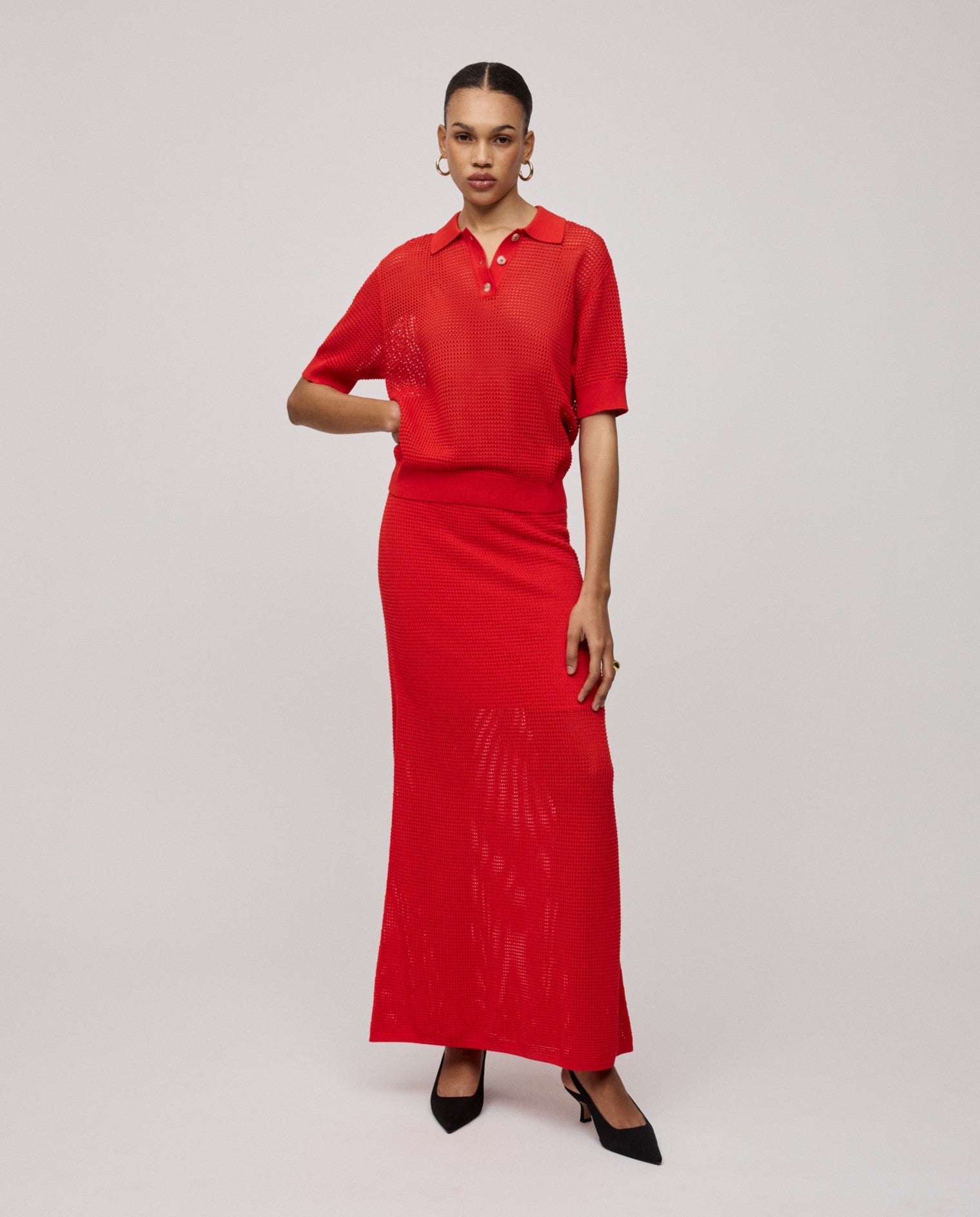 Model wears the IVY OAK FABRIZIA Skirt and a bright red open knit short-sleeve top with black heels, standing against a plain background.