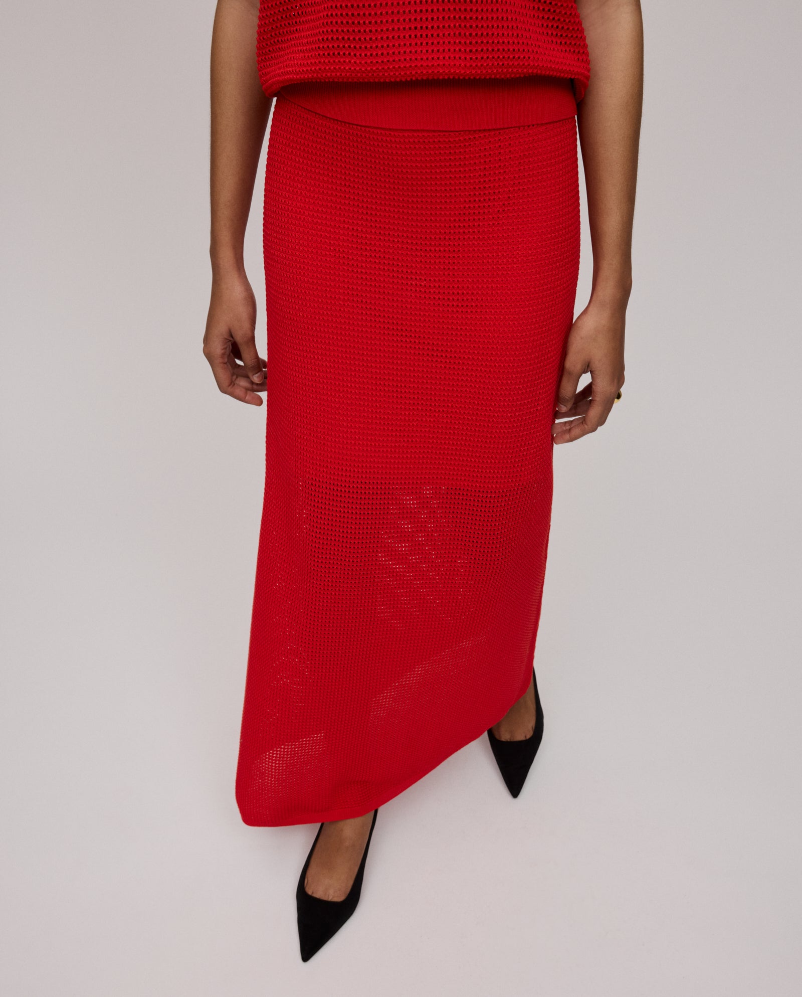A woman wears the IVY OAK FABRIZIA Skirt, a long red knit design with a light A-line silhouette, paired with black pointed-toe shoes, photographed from above for a breezy summer knit look.