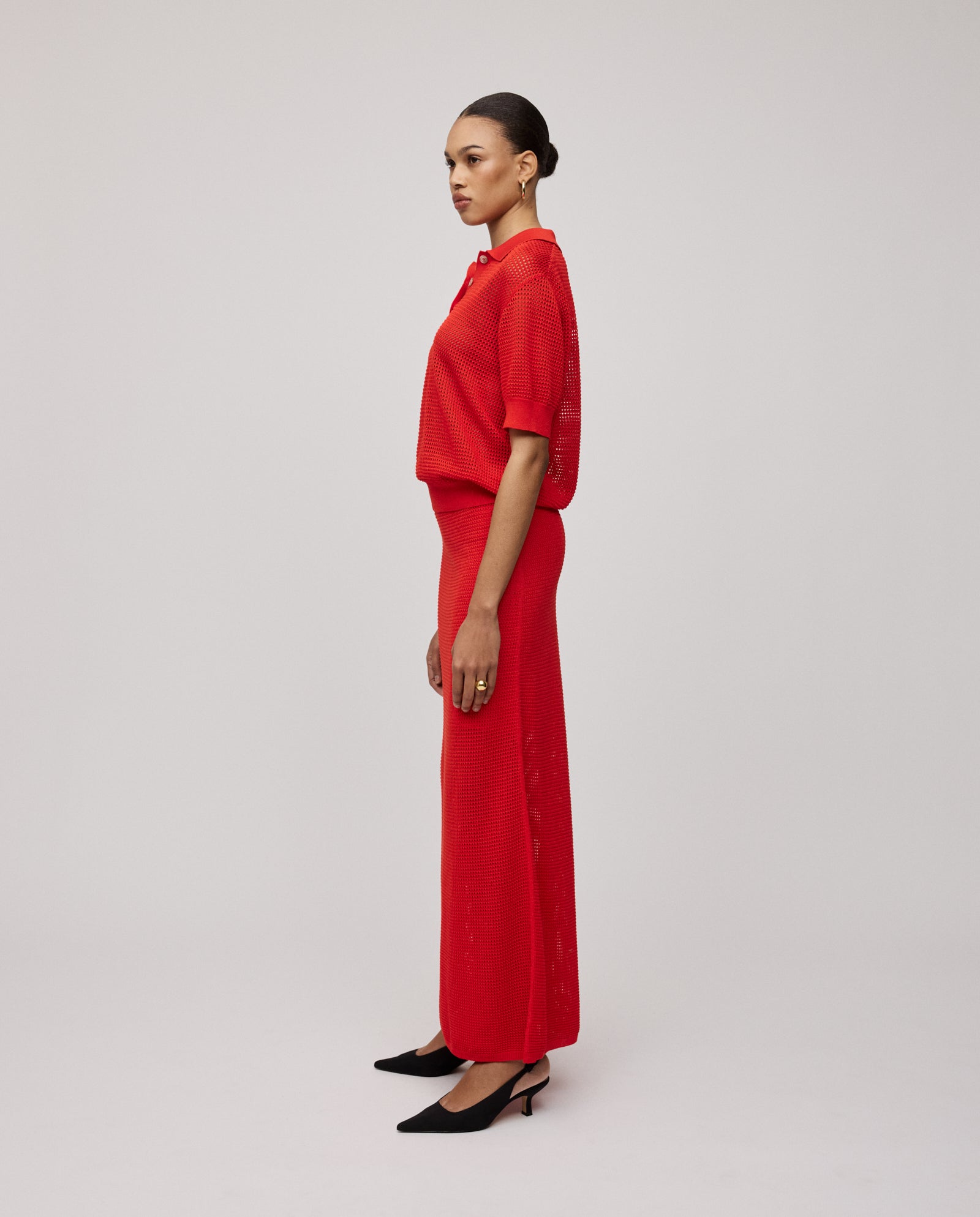 A woman in a red blouse and the IVY OAK FABRIZIA Skirt, featuring a light A-line silhouette, wears black heels and stands in profile against a plain background.
