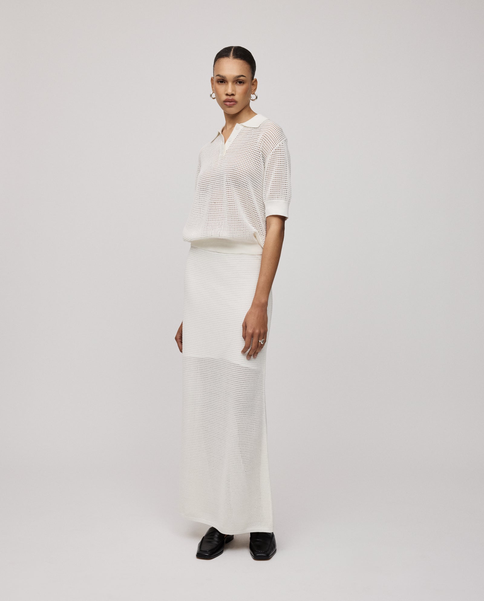 Woman in a sheer white polo shirt and IVY OAK FABRIZIA Skirt with an A-line silhouette, standing against a plain light background.