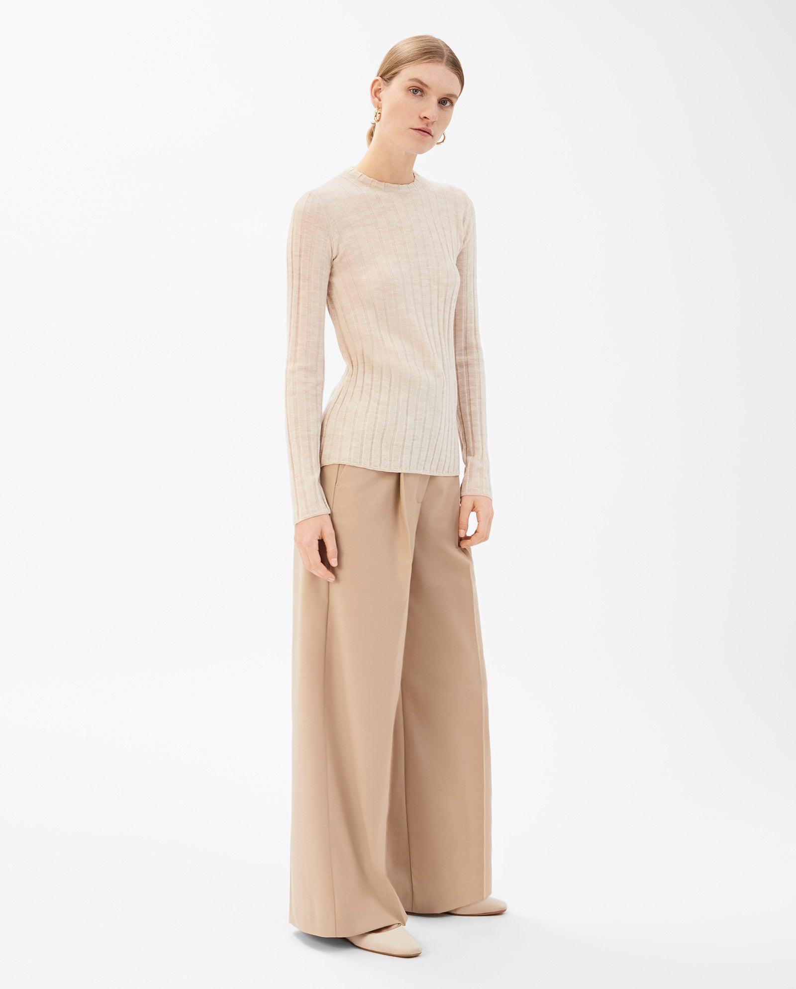 A woman wears the IVY OAK KACY ANN Knittop in beige with wide-leg tan trousers, standing against a white background—an effortlessly chic look for the transitional season.