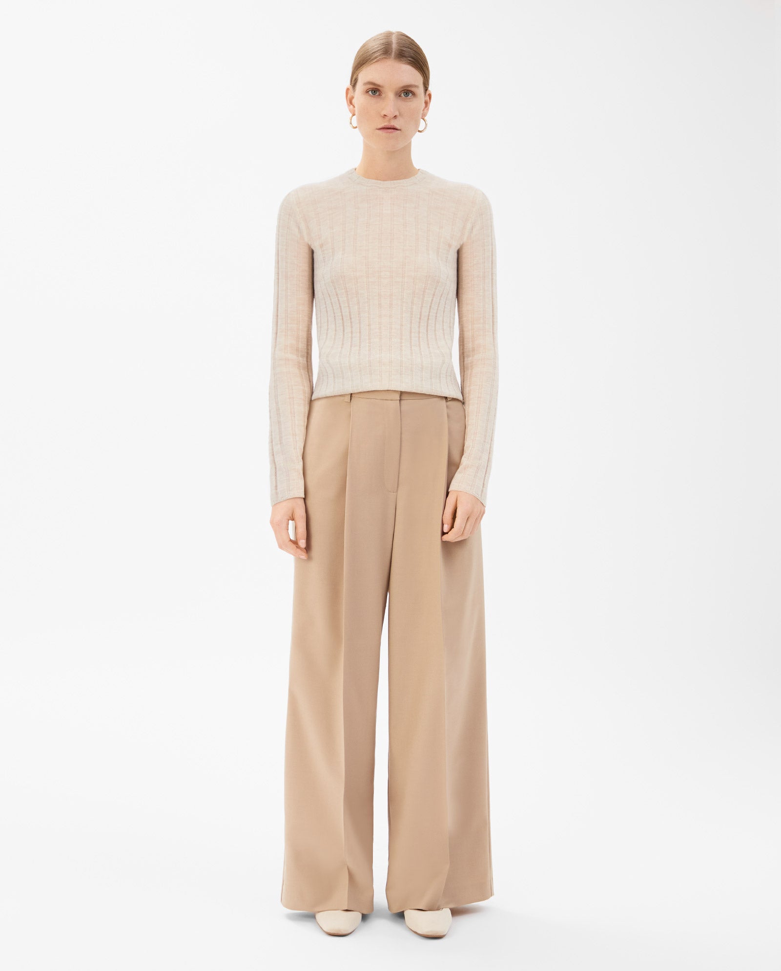 A woman wears the IVY OAK KACY ANN Knittop in beige with wide-leg tan trousers, standing against a plain white background—an effortlessly chic look for the transitional season.