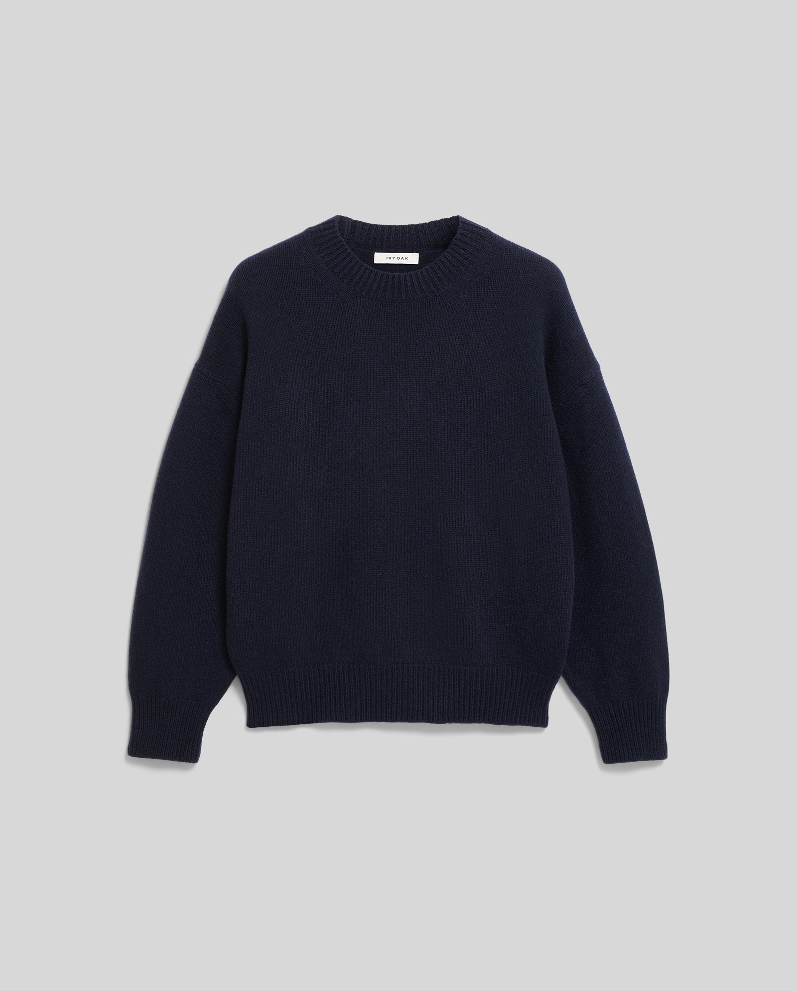 The KASSIDY Jumper by IVY OAK is a navy blue crewneck sweater with long sleeves and an oversized fit, shown against a light gray background for a cozy vibe.