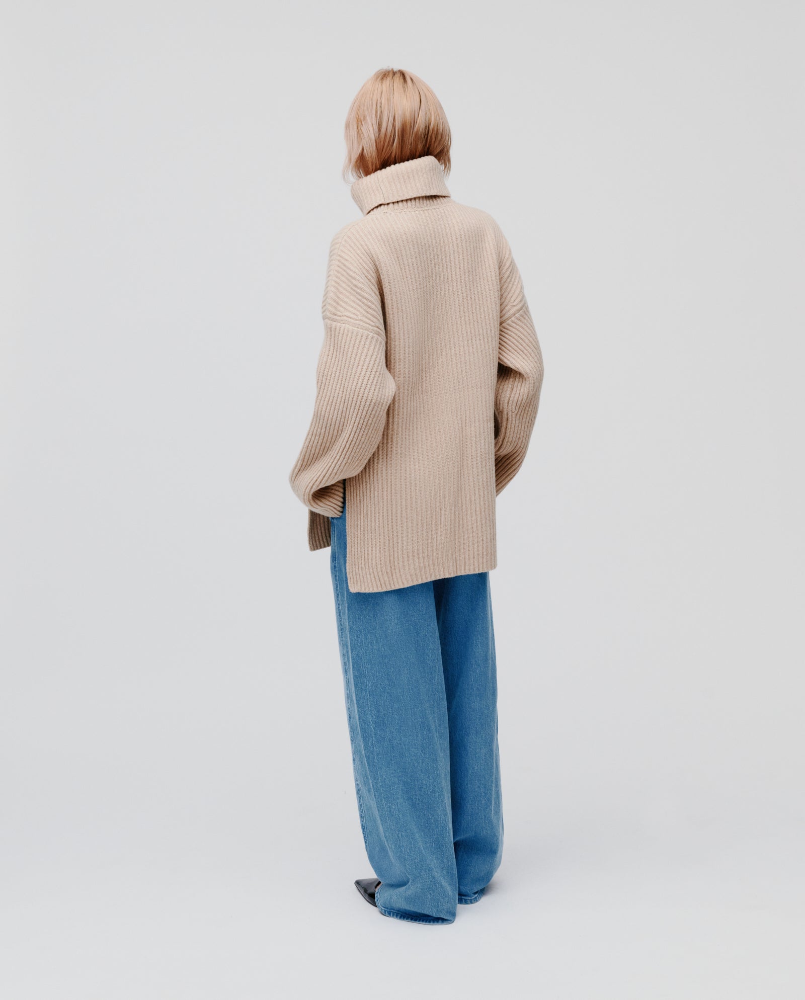 Person with short blonde hair, seen from behind, wearing the IVY OAK KYOMI ANN beige jumper and blue jeans.