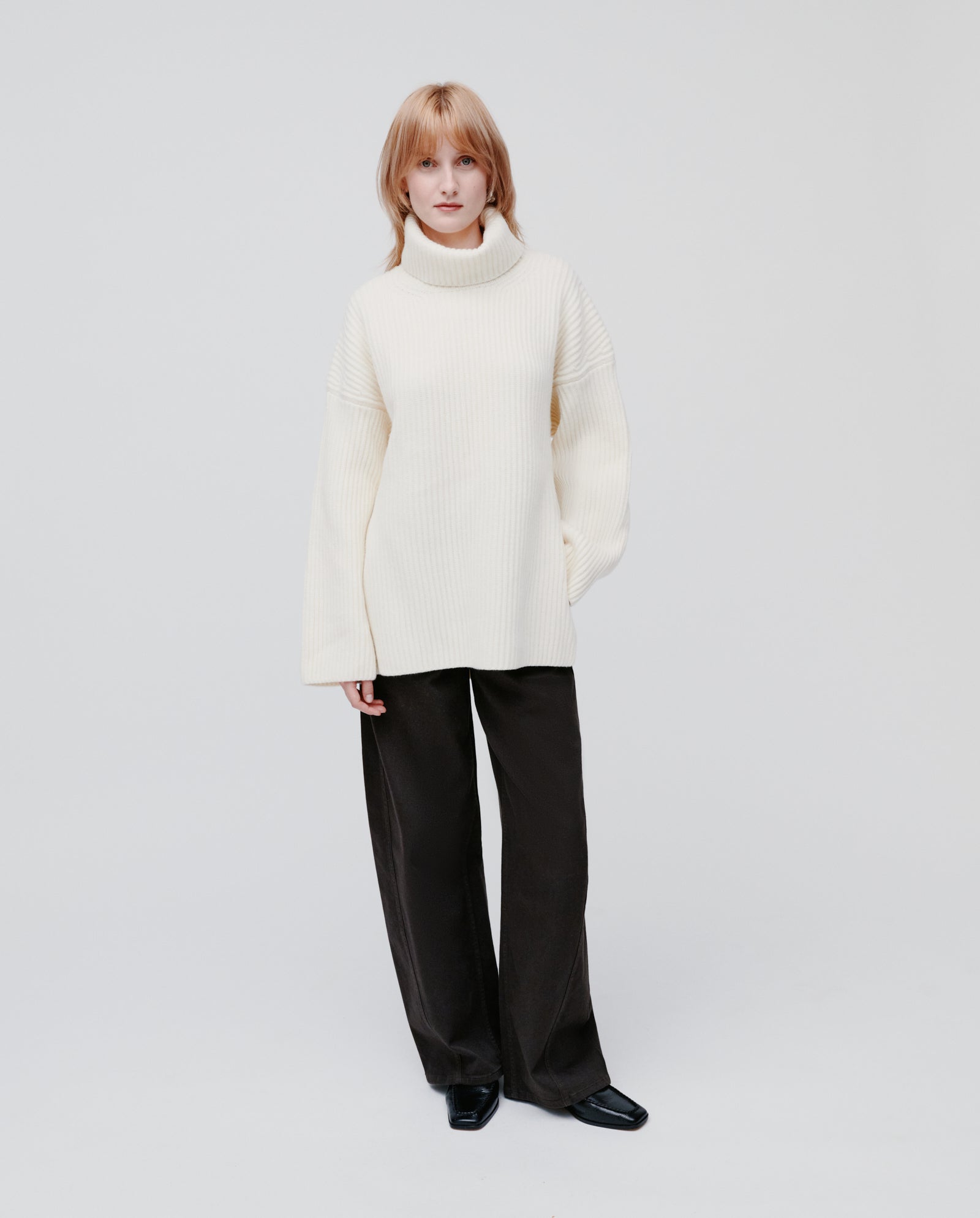 Model wears the IVY OAK KYOMI ANN jumper in cream with loose black pants, standing against a plain light background.